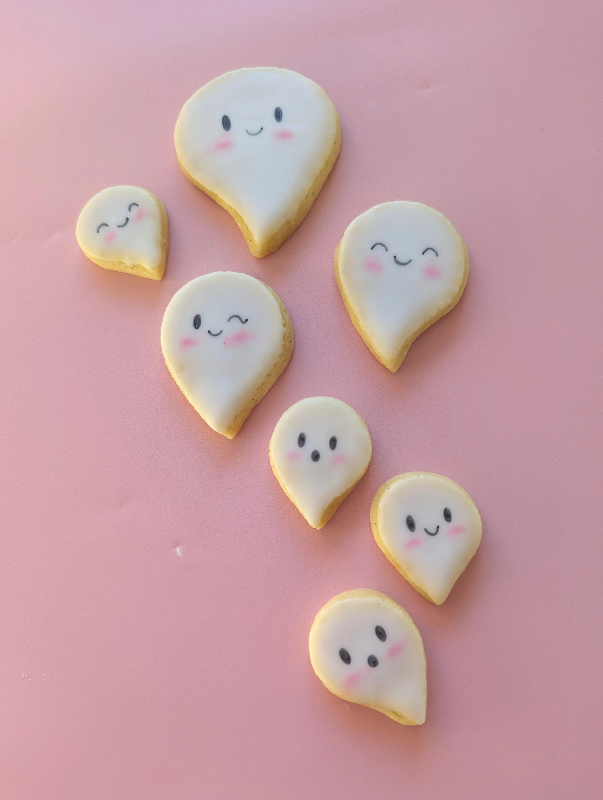 several small sugar cookies decorated as ghosts on a light pink background