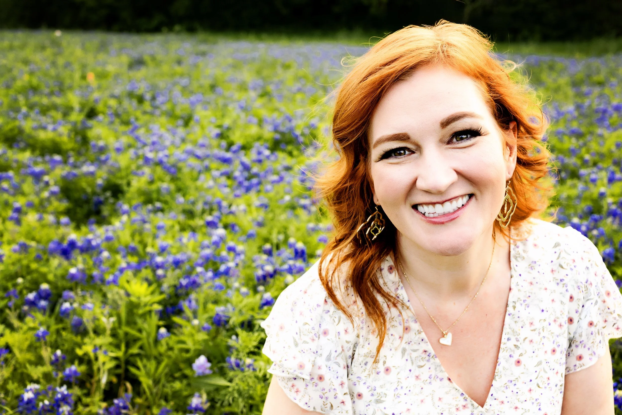 Red head woman with bright smile sitting in a field of flowers