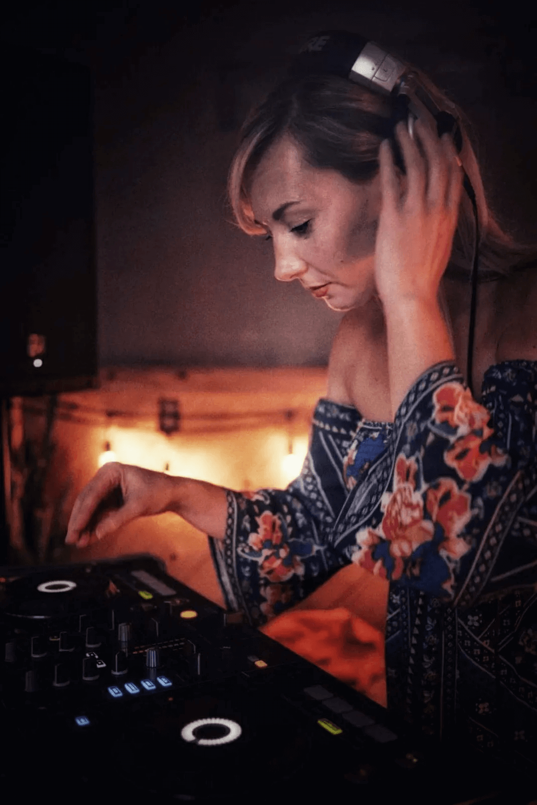 DJ Angie Spence adjusting her mixer with headphones on in a dim venue