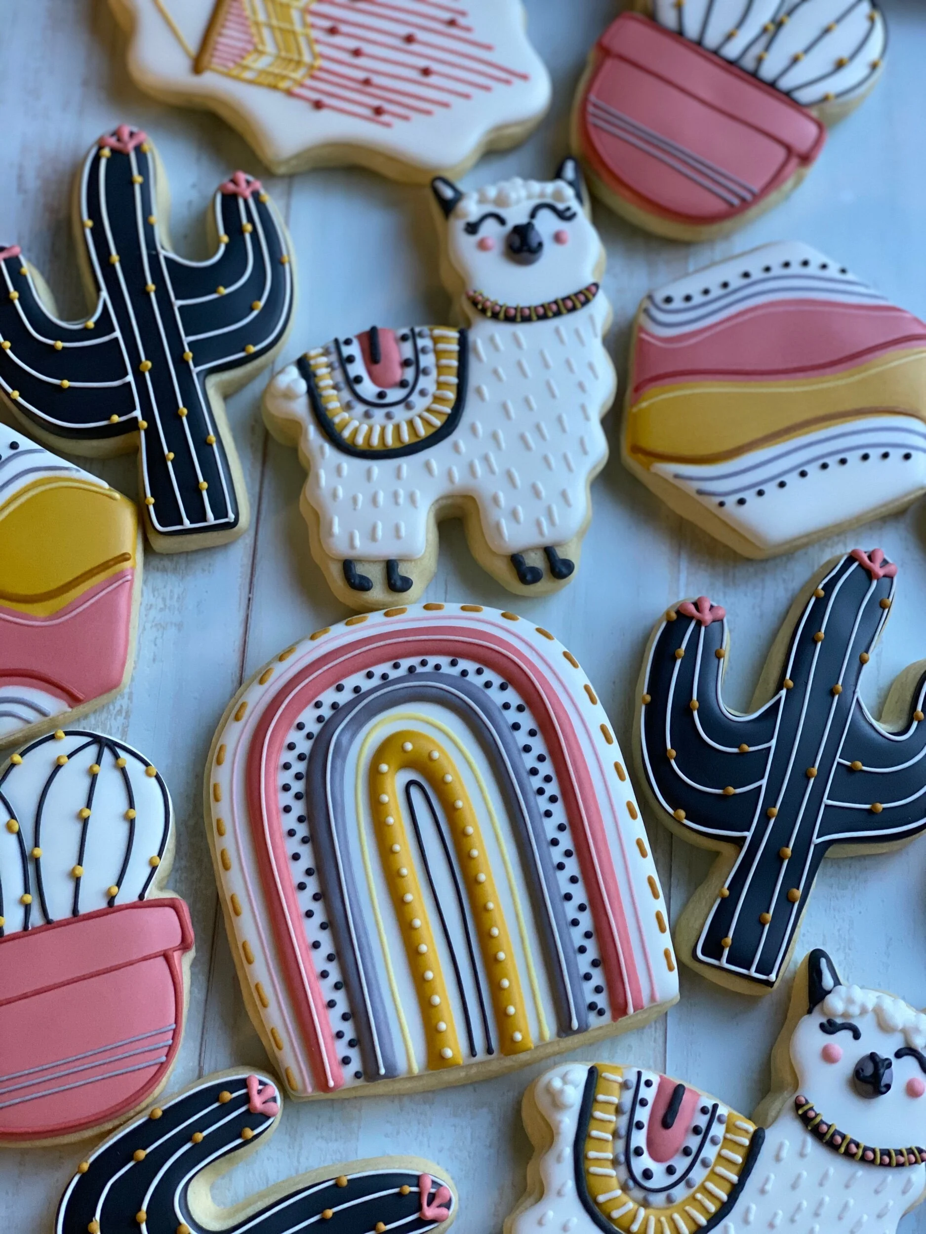 Decorative cookies shaped like a cactus, a llama, and abstract patterns with colorful icing and sprinkles.