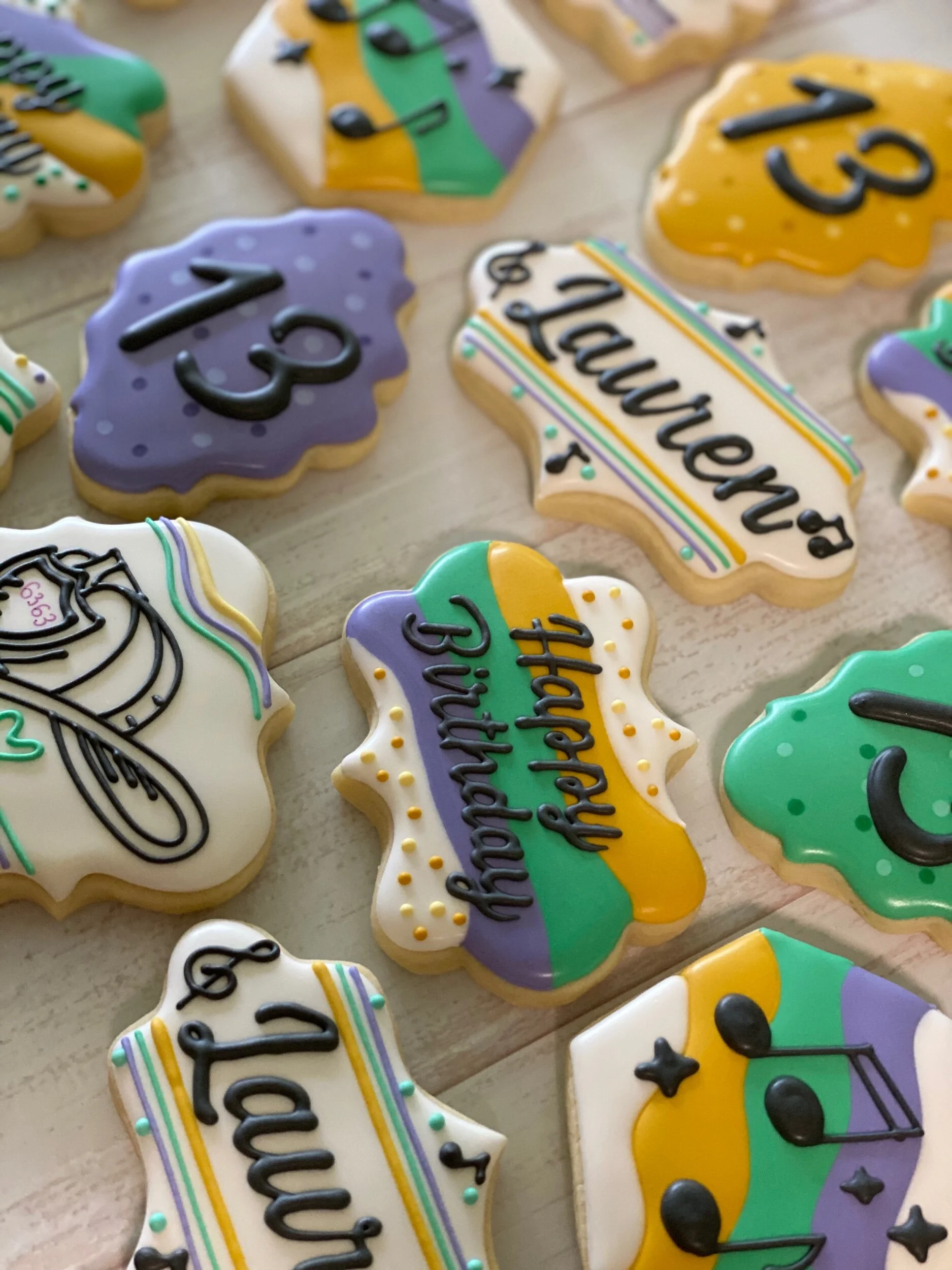 Assorted decorated sugar cookies with birthday messages, including 'Happy Birthday' and 'Love,' in colorful icing with various patterns and embellishments.