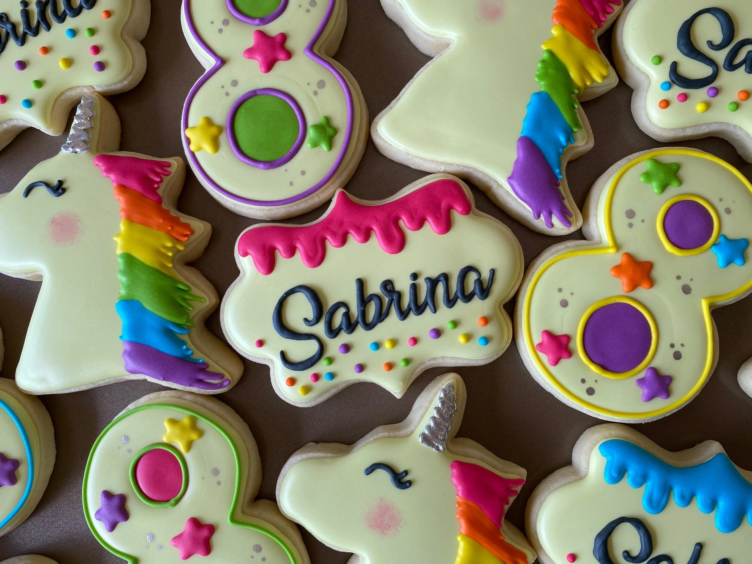 Colorful decorated cookies including stars, unicorns, and other shapes with bright icing and sprinkles.