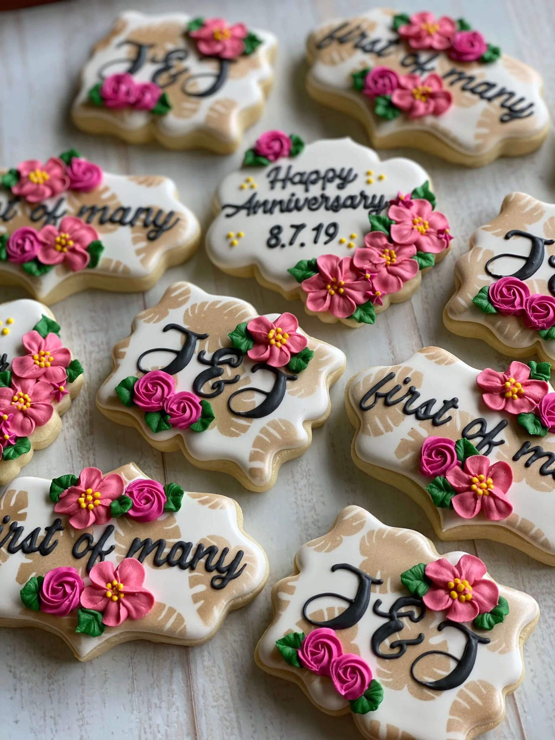 Decorated cookies with floral designs and message for a 50th wedding anniversary celebration, featuring pink flowers, green leaves, and black icing writing.