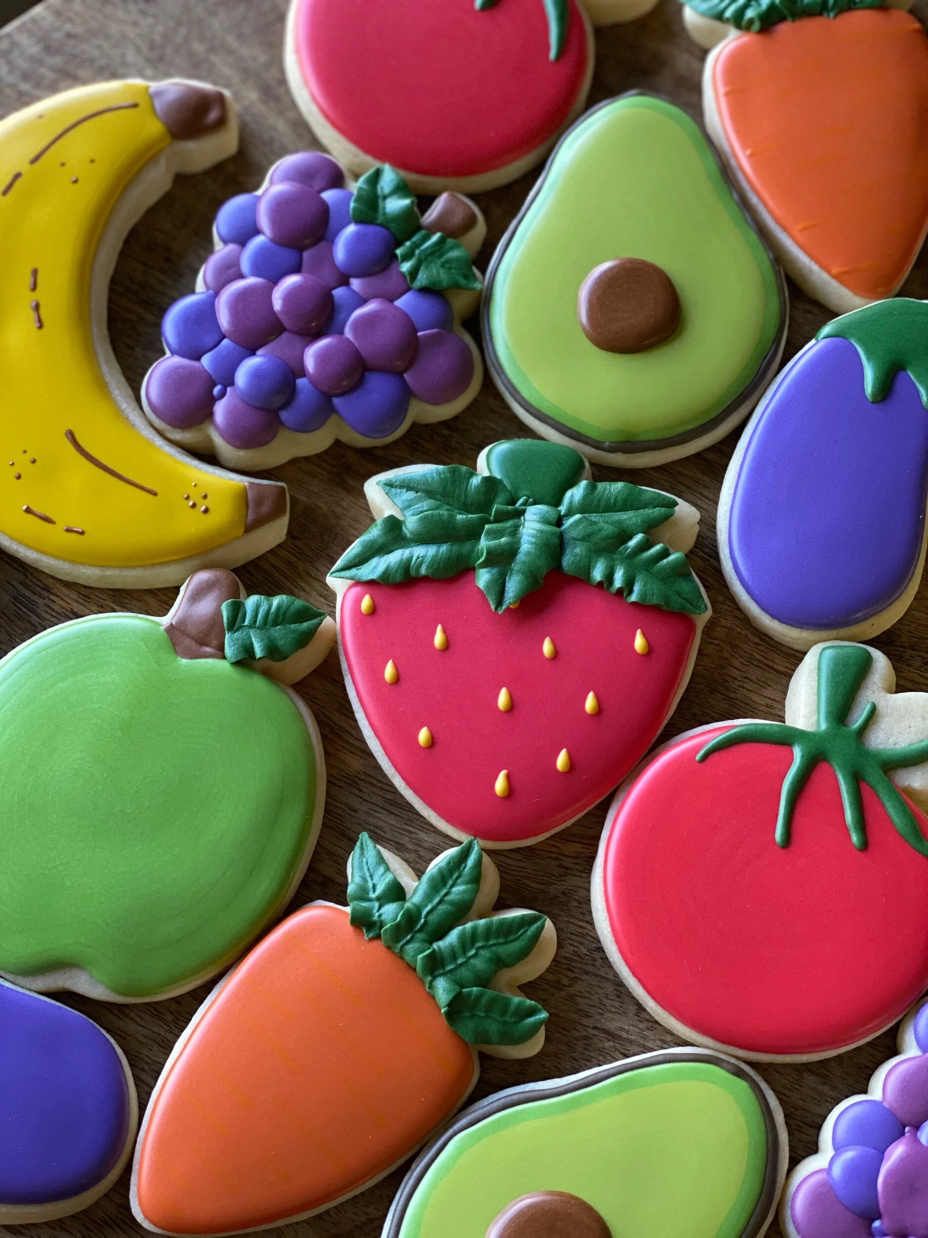 Colorful decorated cookies shaped like fruits, including bananas, grapes, strawberries, and avocados.