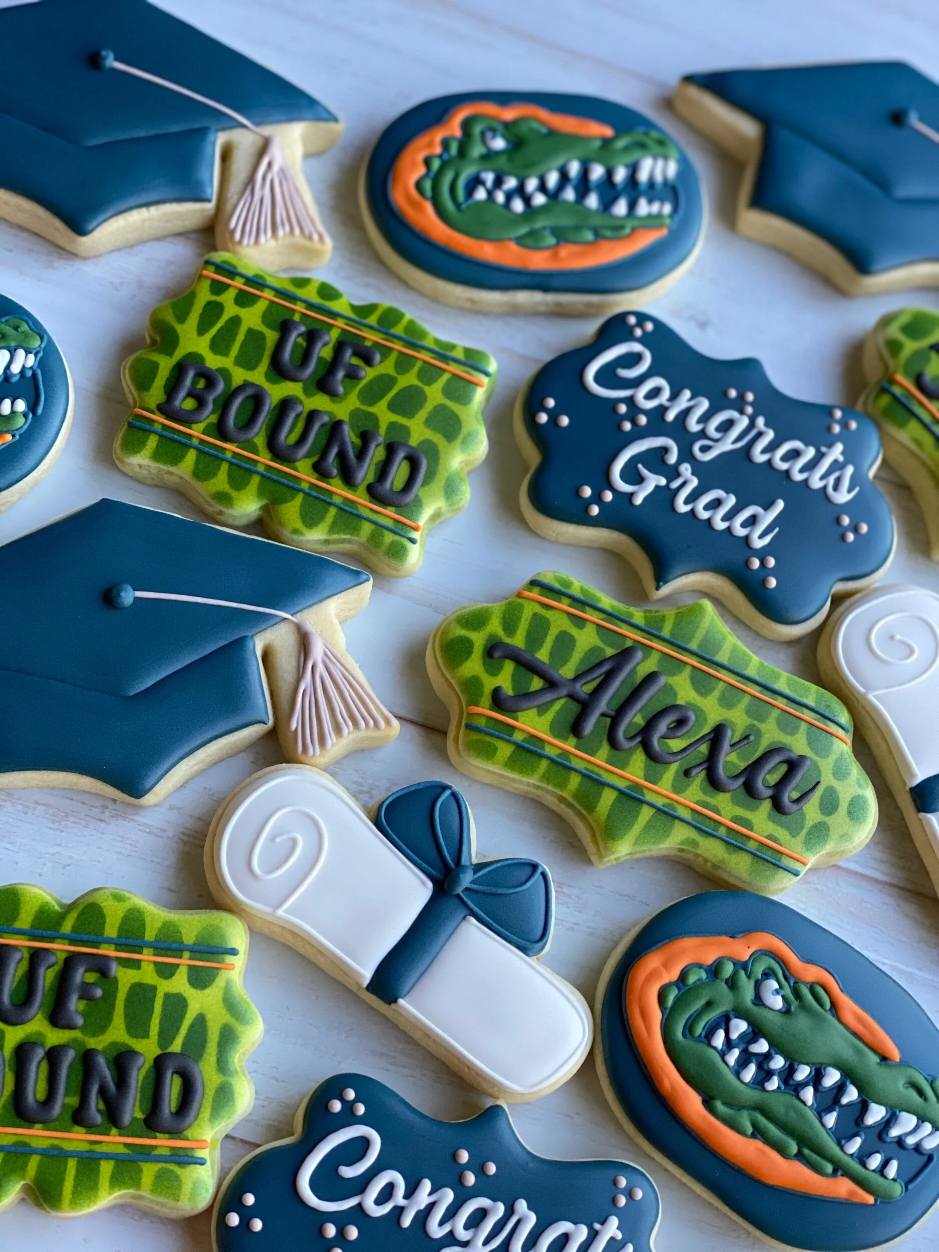 Cookies decorated with college graduation theme, including diplomas and phrases like 'Ucf Bound' and 'Congratulations Grad', in blue, green, and orange icing.