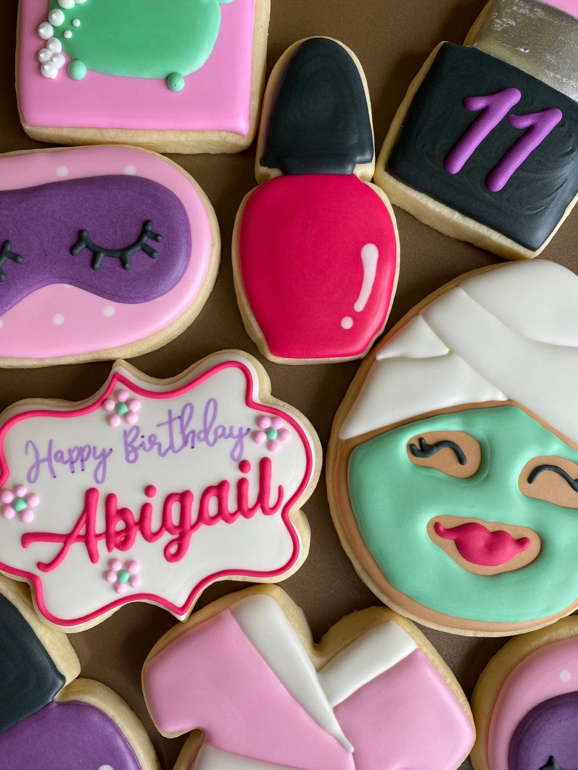 Decorated cookies for a birthday celebration, featuring various colors and designs including a message that says 'Happy birthday Abigail' and a number '11'.