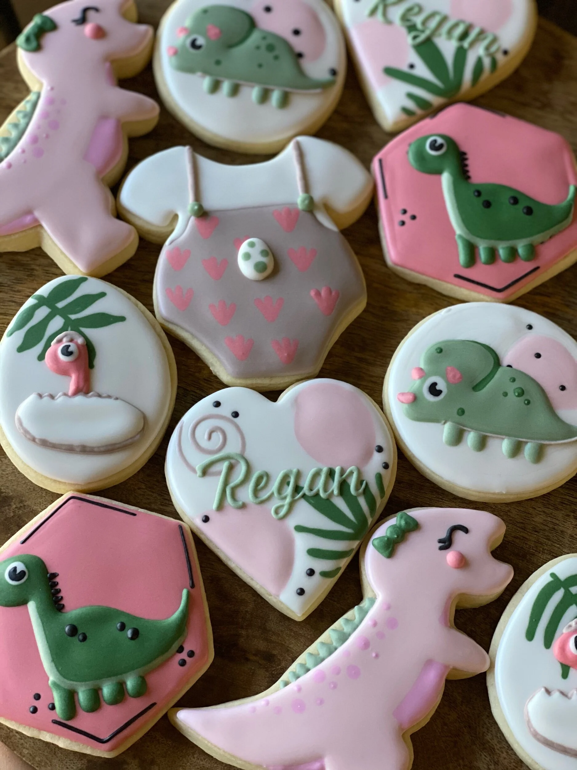 Decorated cookies with dinosaur and nature themes, some with the word 'Relax' and 'Dream,' featuring pastel pink, green, and white icing.