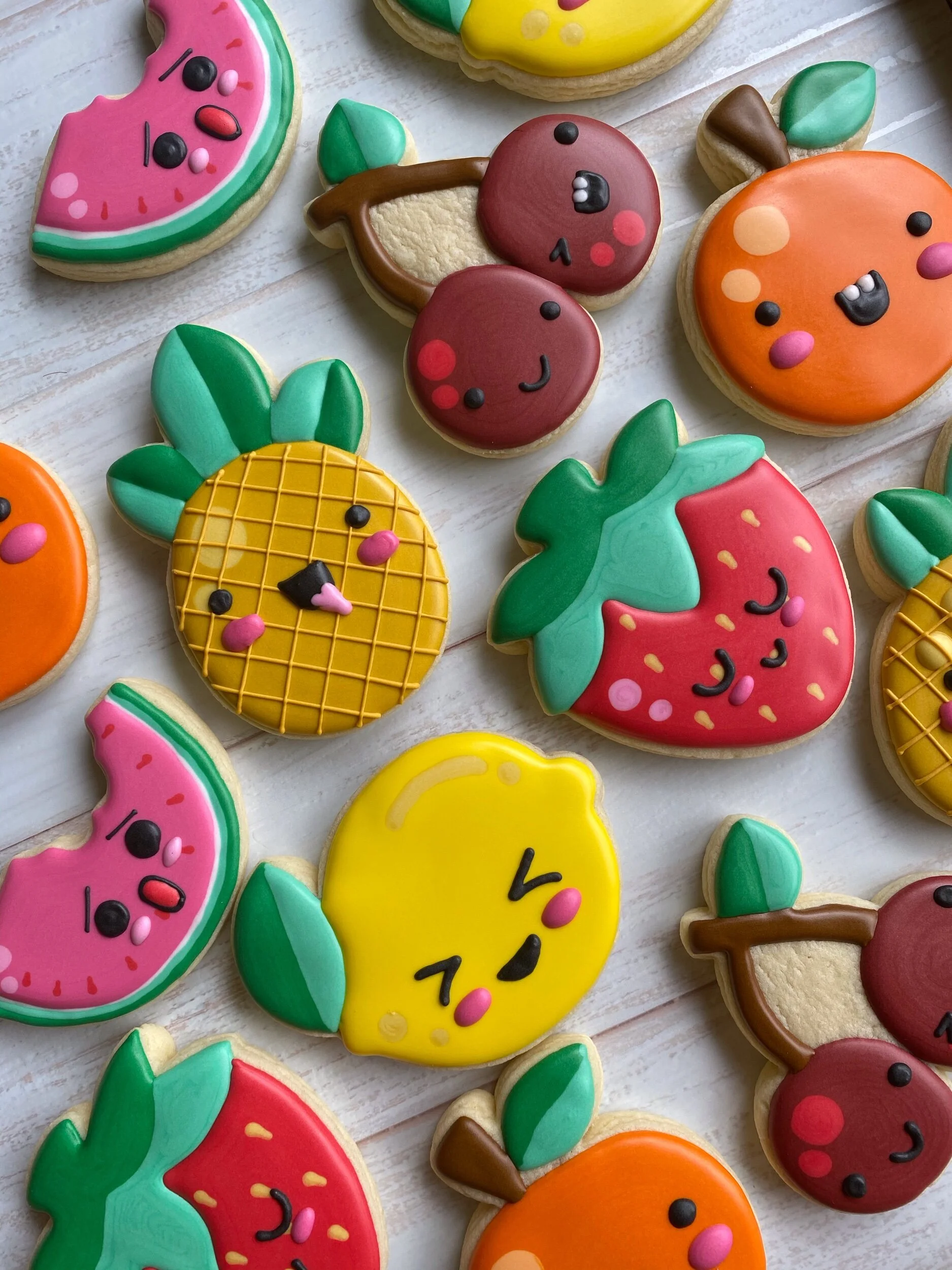 Colorful animal-shaped sugar cookies decorated with vibrant icing, featuring various fruits such as watermelon, cherry, pineapple, strawberry, and orange.
