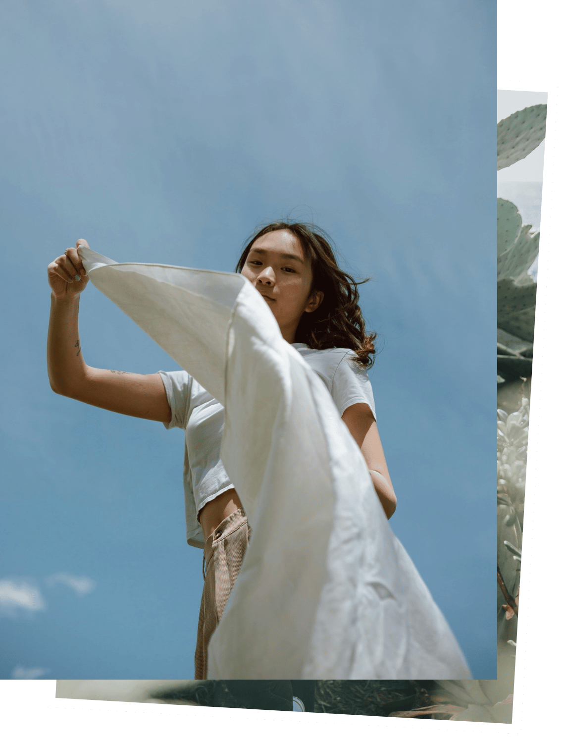 Young woman holding a white cloth or blanket outdoors with a blue sky background.