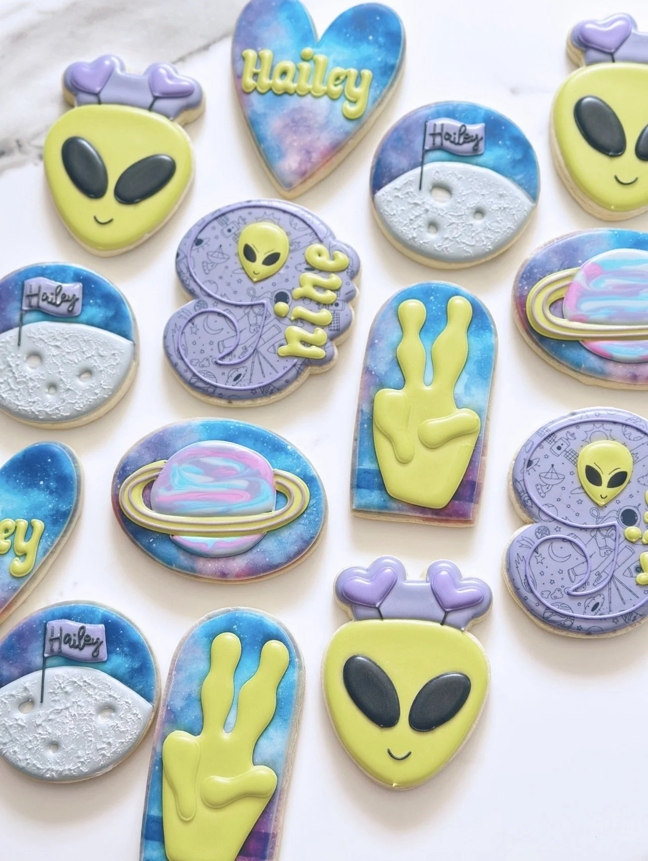 Colorful decorated sugar cookies with alien, space, and moon themes, some with the name 'Hailey' on them.