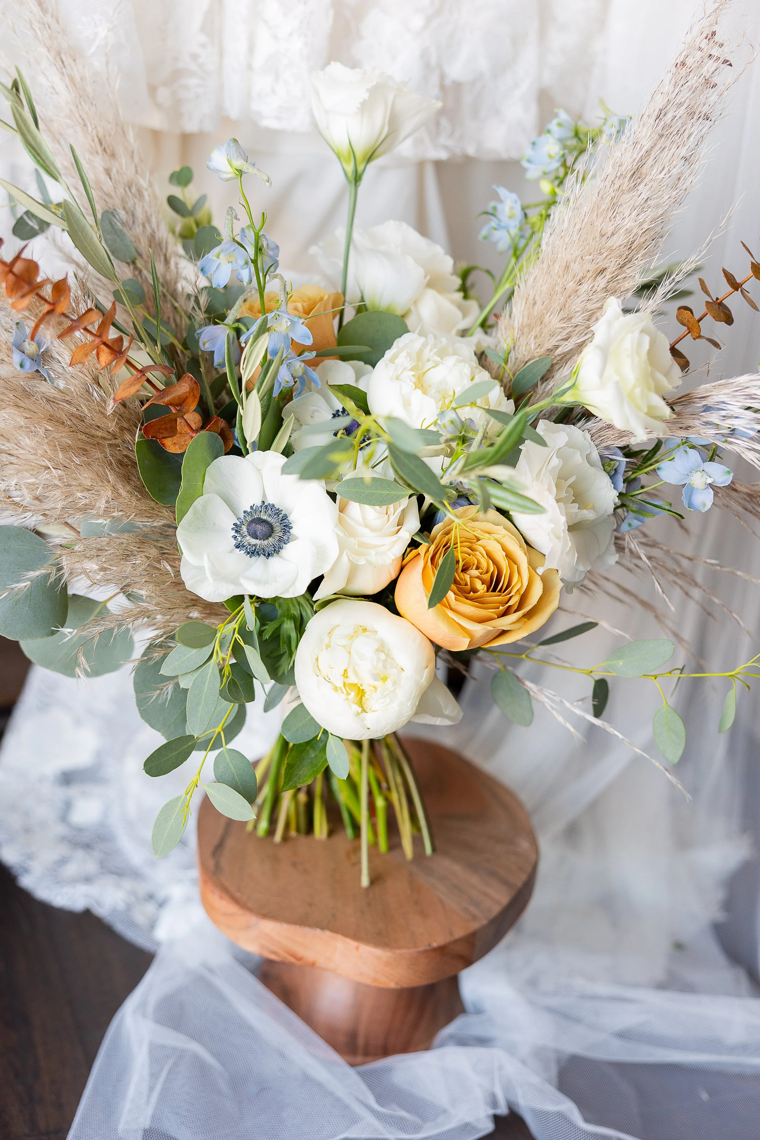 Bridal bouquet made of pampas grass, aneone, toffee rose, delphinium and eucalyptus on a wood round, sonora florist