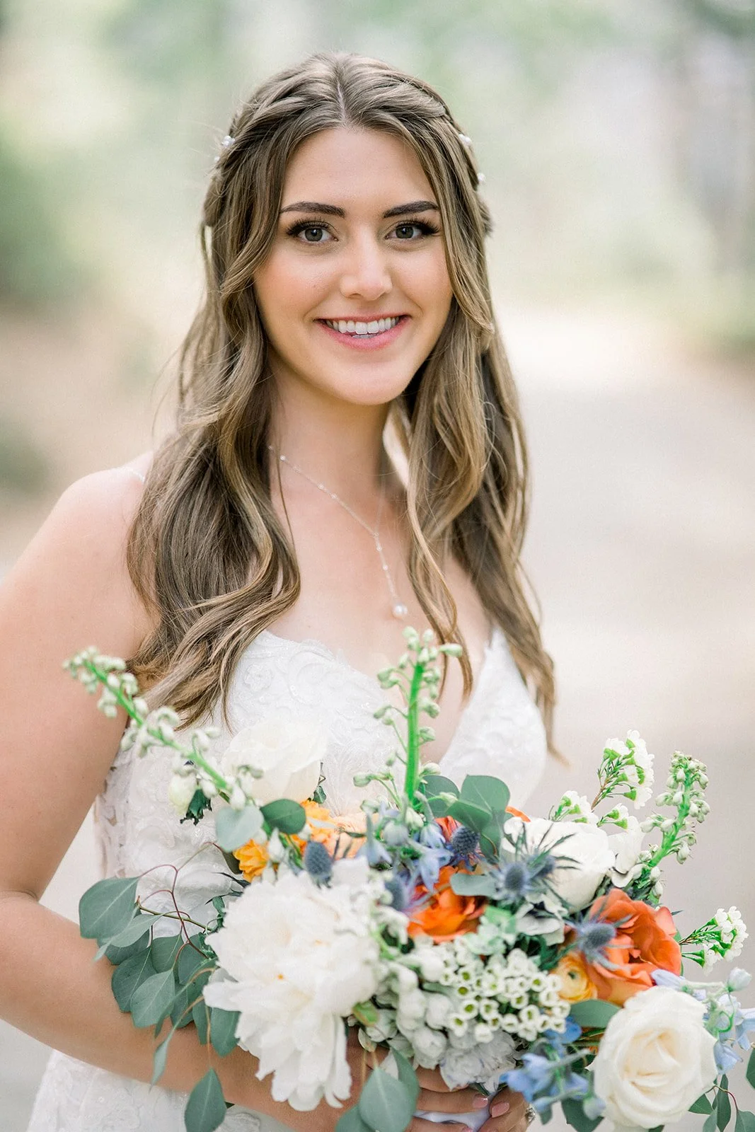 Brunette bride smiling while holding her bridal bouquet made of white, orange, and blue flowers, sincerely sonora florist