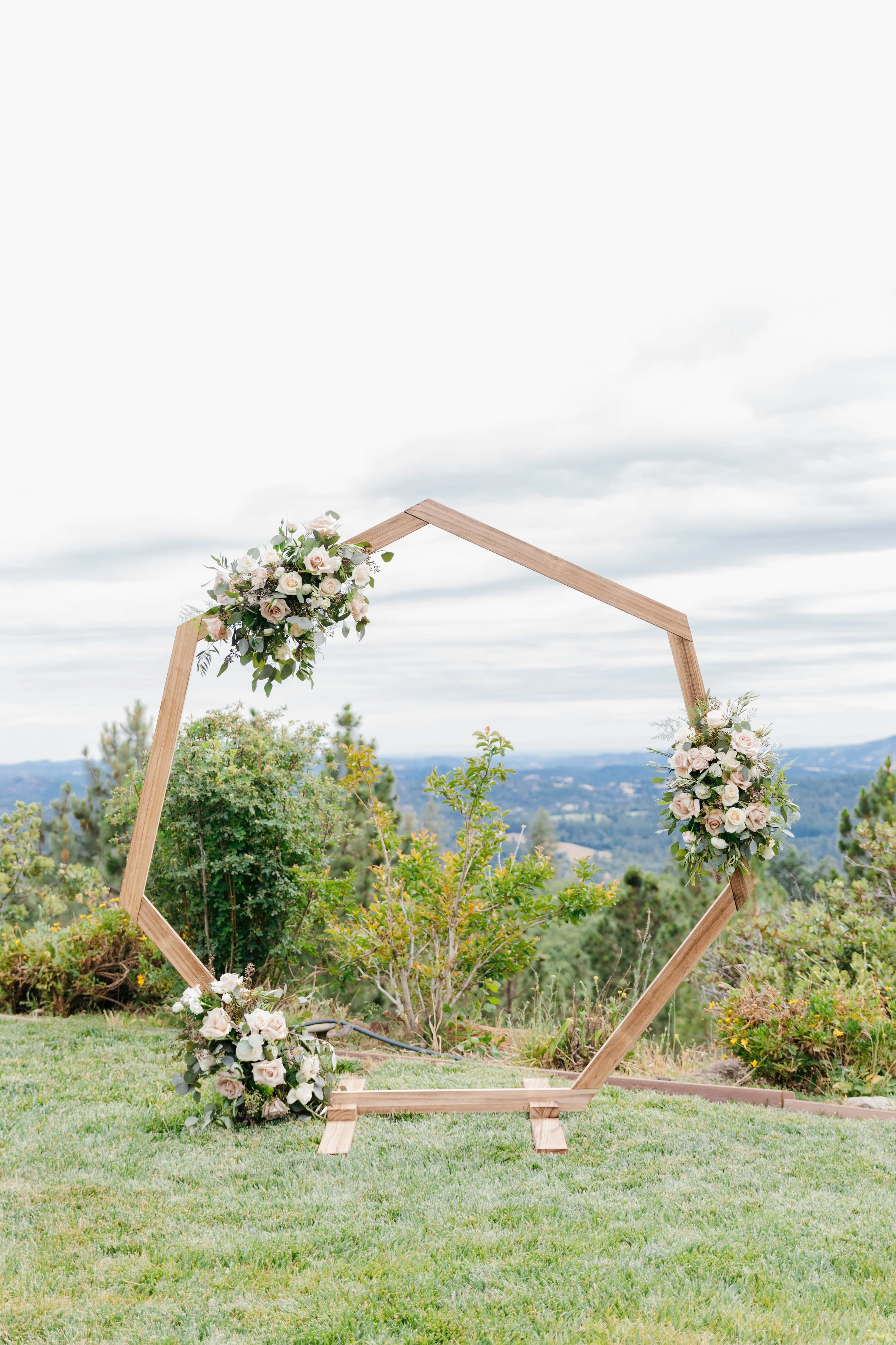 Hexagon arch with three floral pieces on it made of quicksand roses, pray roses, white ranunclus, eucalyptus, and plumosa, calaveras county wedding flowers