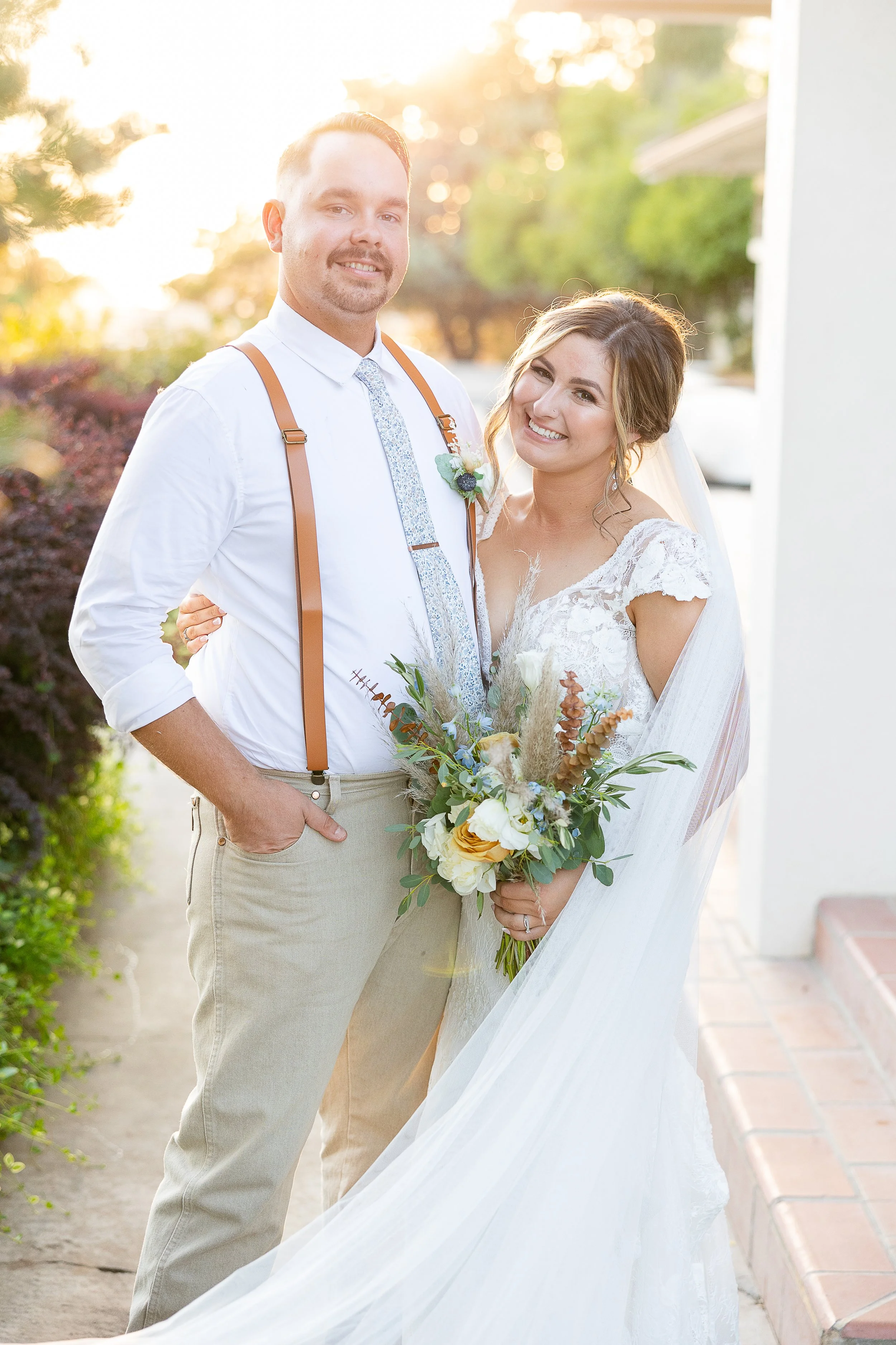 bride and groom smiling infront of the sunset while holding bridal bouquet made of anemone, toffee roses, pampas grass, eucalypus, sincerely sonora florist
