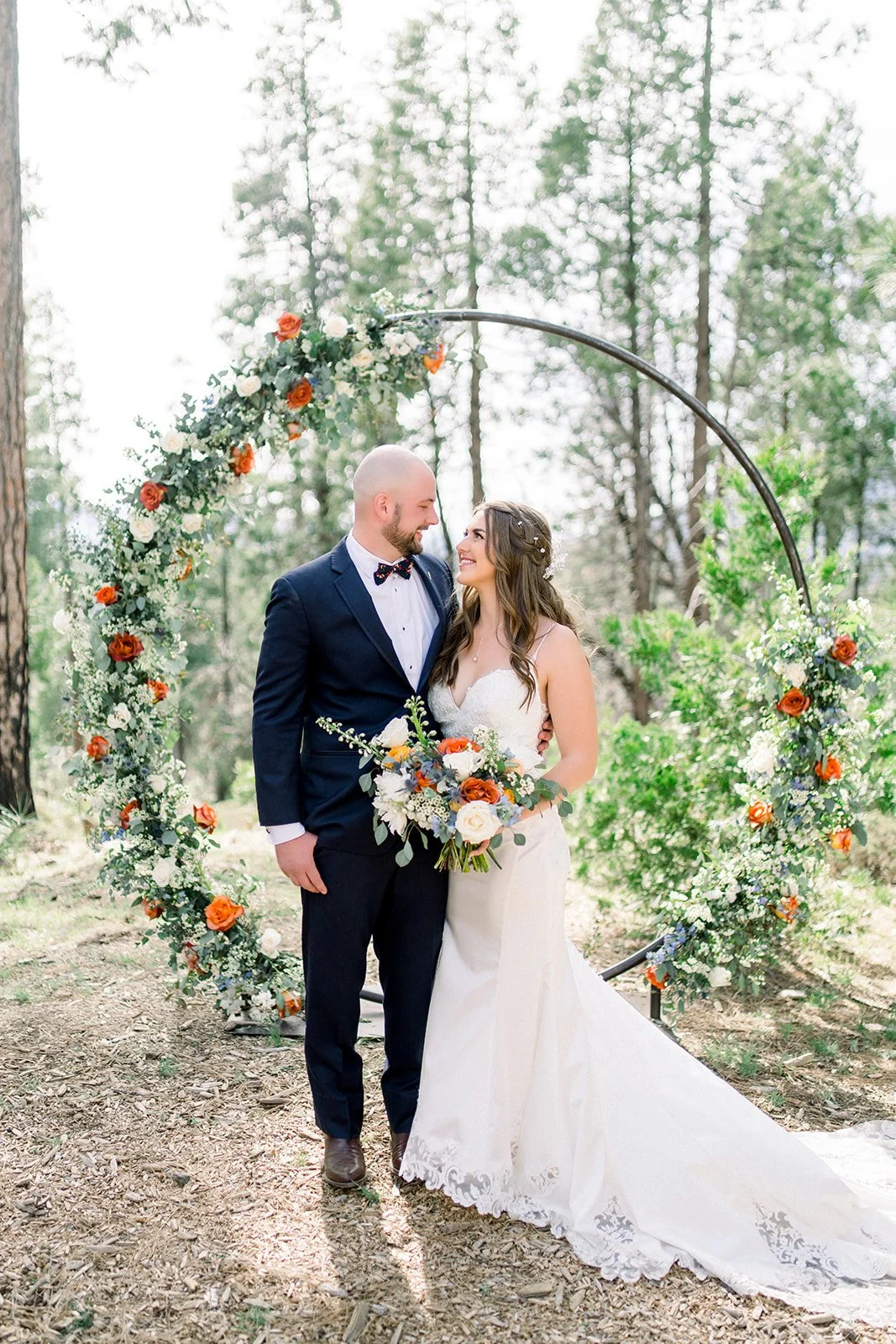 Bride and groom smiling in front of a round floral arch while she holds her bridal bouquet, rushcreek lodge