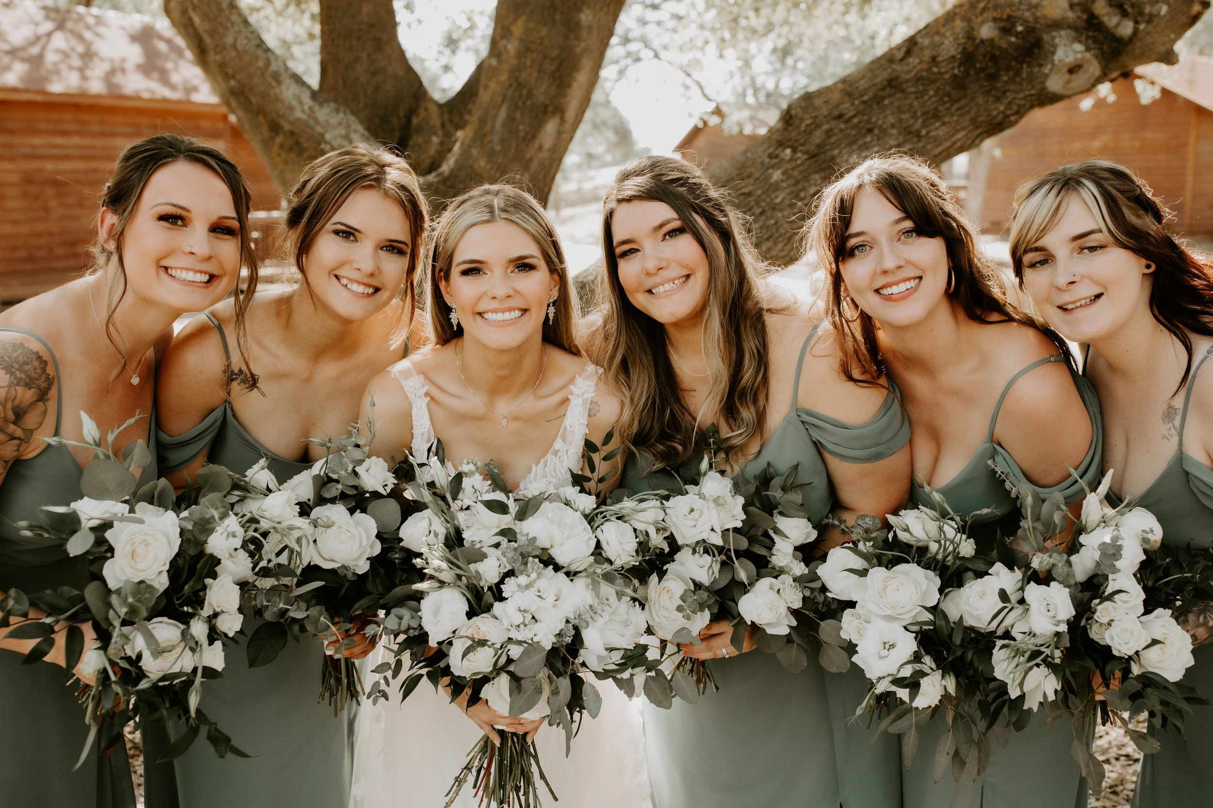 Bridal party all smiling and holding white bouquets made of peonies, lisianthus, ranunculus, roses, and spray roses, sonora ca wedding flowers