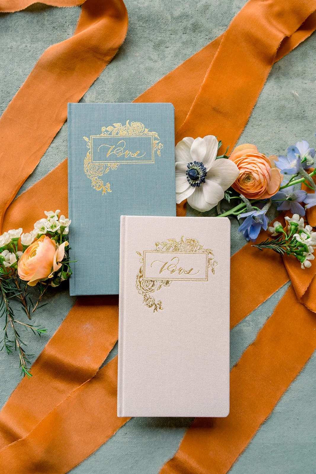 Bride and groom books with orange ribbon and a mix of anemones delphinium and ranunculus, sincerely sonora florist