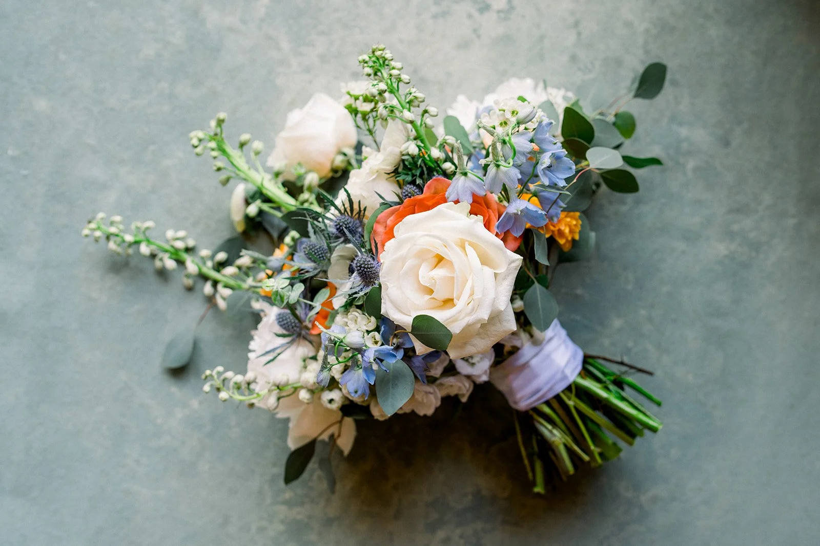 Orange, white and blue bridal bouquet with roses, delphinium, eryngium, and ranunculus, groveland ca