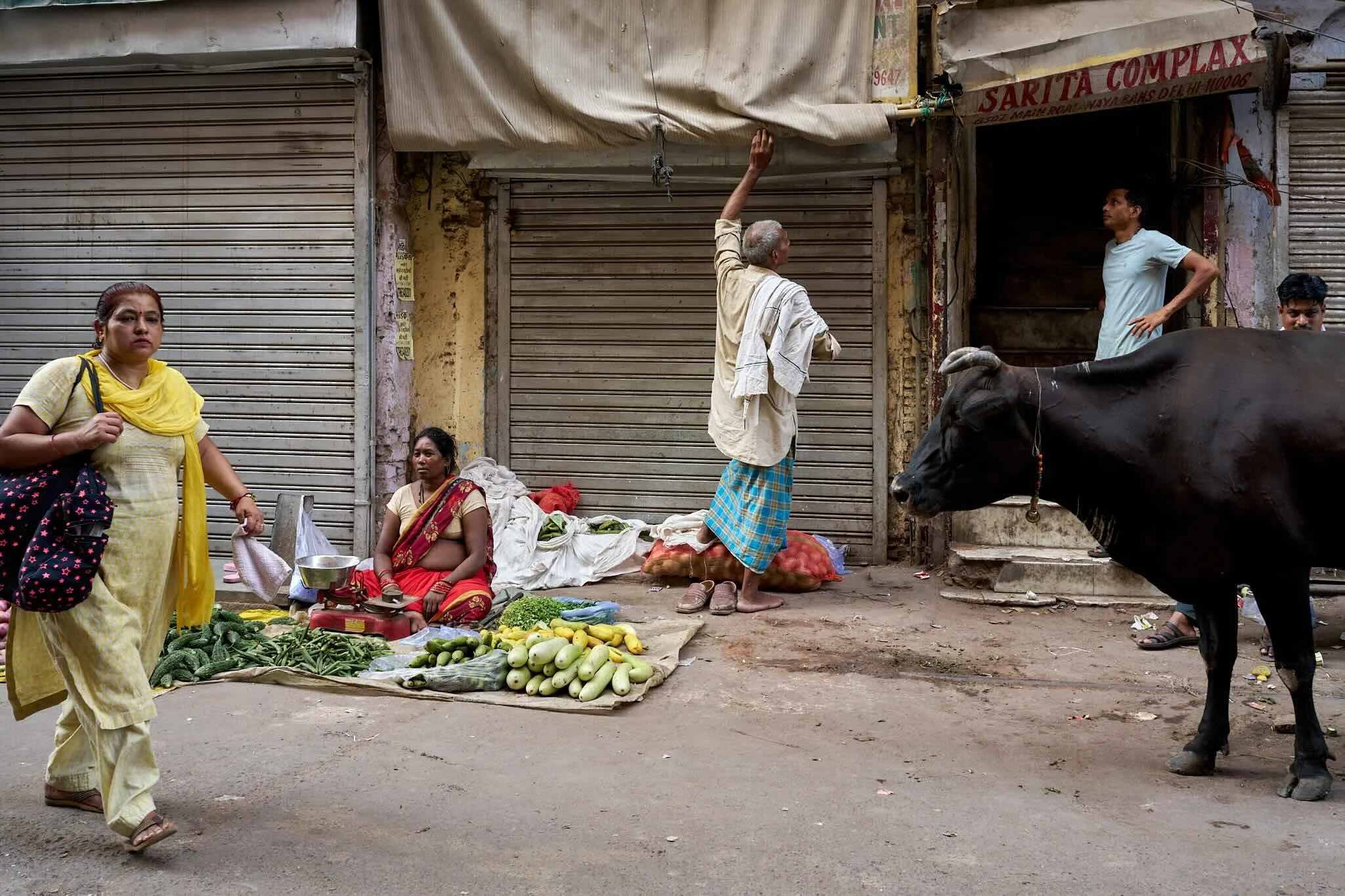Jerzy Jaworek, Street and Travel Photography, India, Delhi. Street market scene in India with vendors selling fresh vegetables on the sidewalk; closed shop shutters in the background.