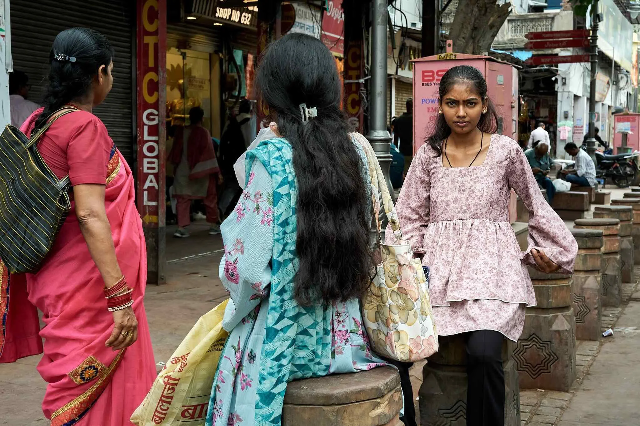 Jerzy Jaworek, Street and Travel Photography, India, Delhi. Four women stand on a busy street, one in a pink sari with black hair tied back, one in a patterned light blue sari with long black hair, 