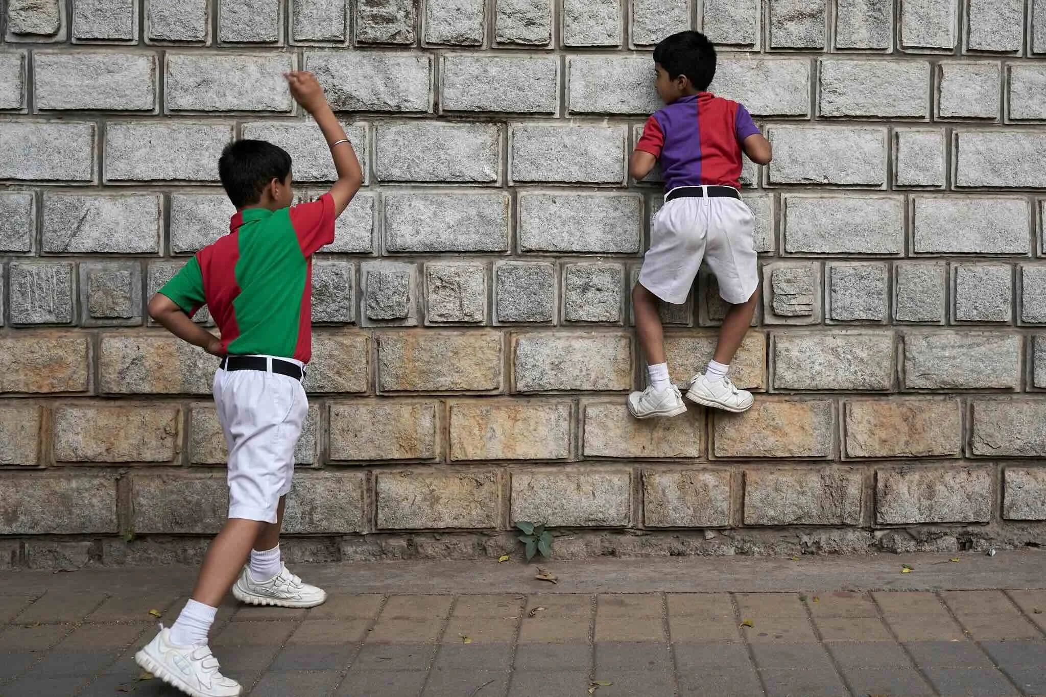 Jerzy Jaworek, Street and Travel Photography, India, Delhi. Two young boys playing outside against a stone wall, one climbing on the wall and the other standing nearby watching.