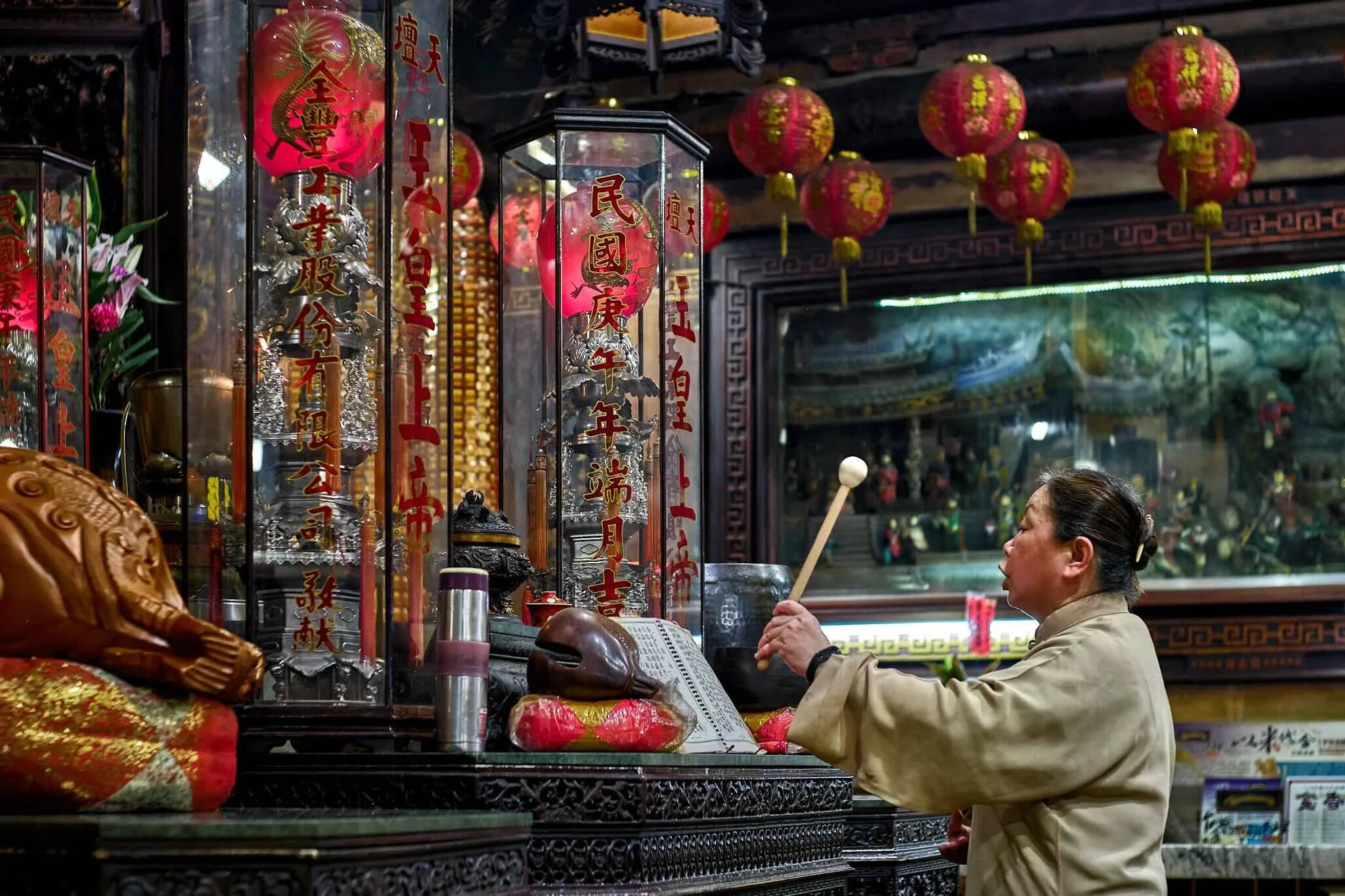 A woman praying inside a traditional Chinese temple, surrounded by red lanterns and Chinese calligraphy displays.