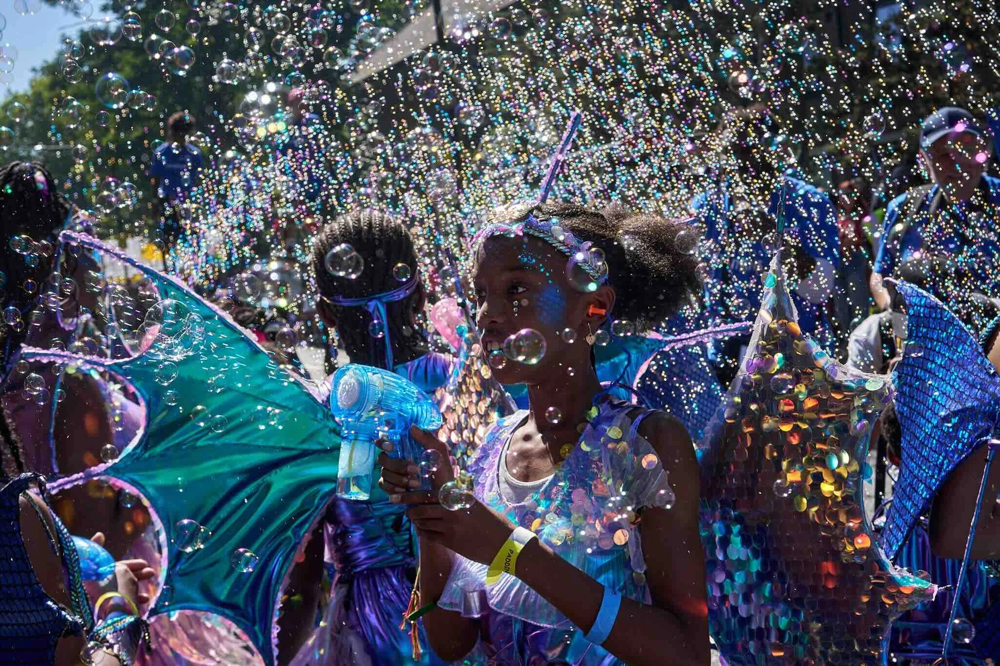 A child amidst a vibrant display of bubbles and confetti during an outdoor event or parade.