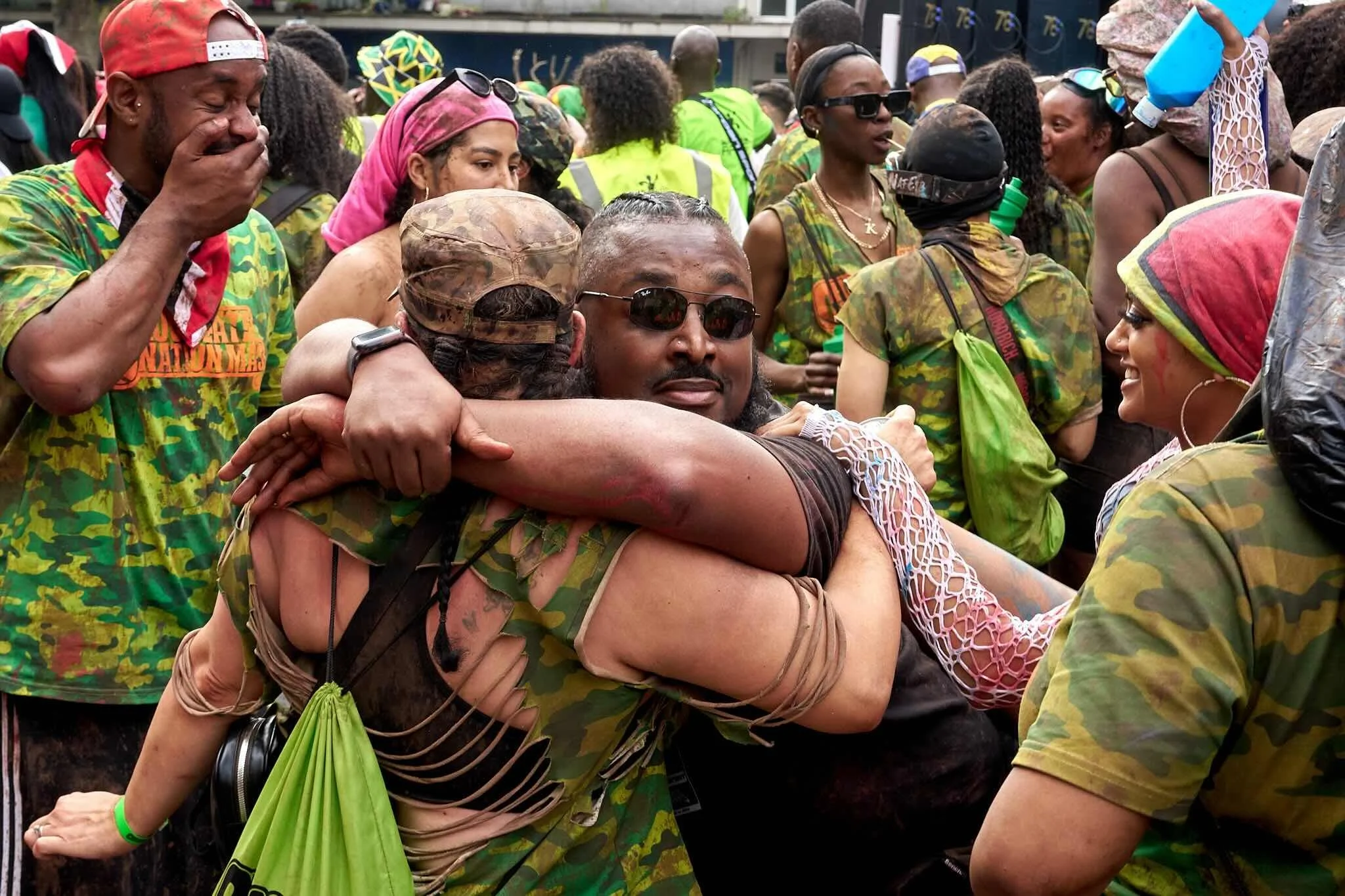 A group of people at an outdoor event, mostly wearing camouflage clothing, with some embracing, smiling, and engaging with each other.