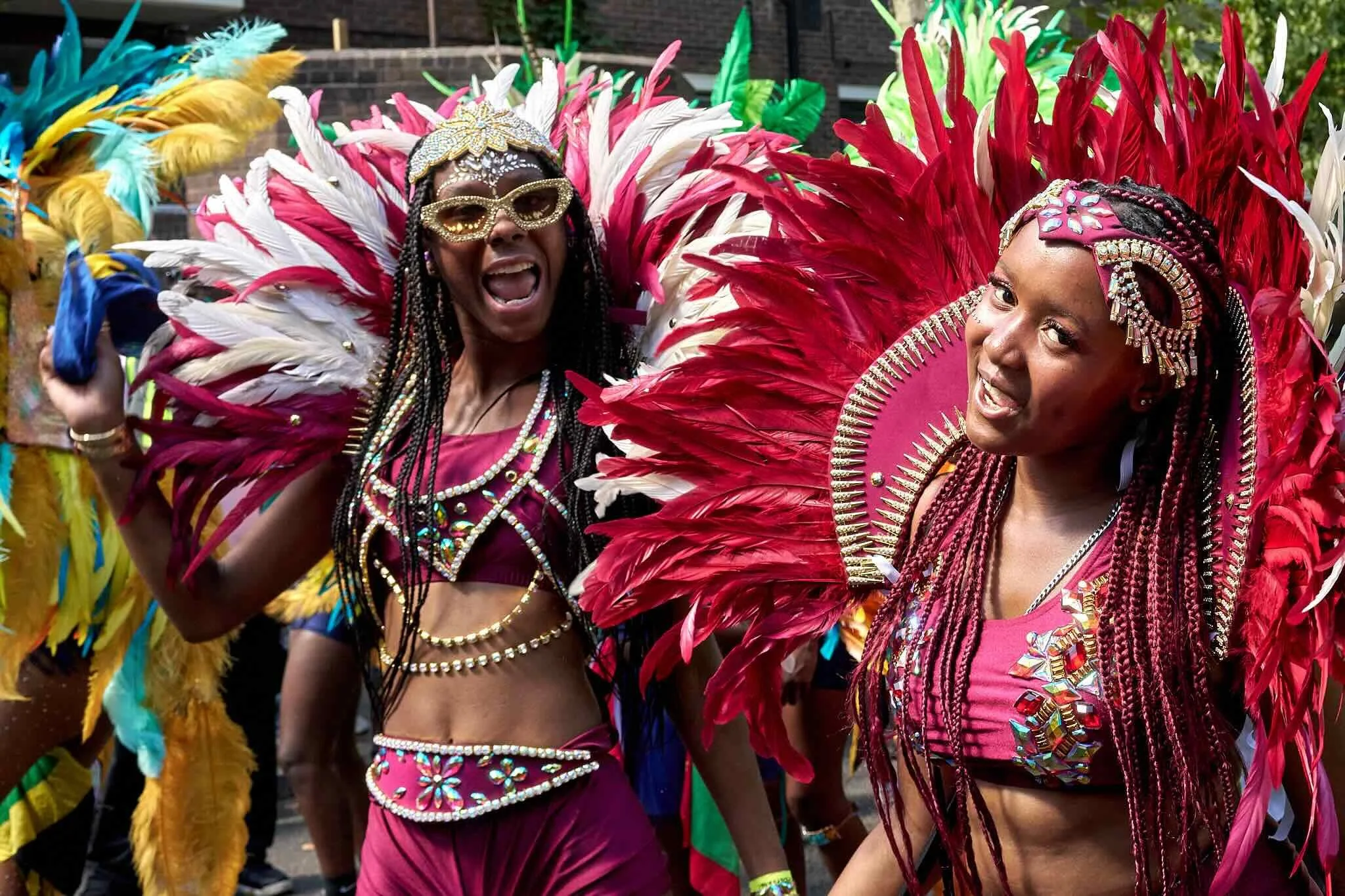 Two women dressed in colorful carnival costumes with large feathered headdresses participating in a parade or celebration.