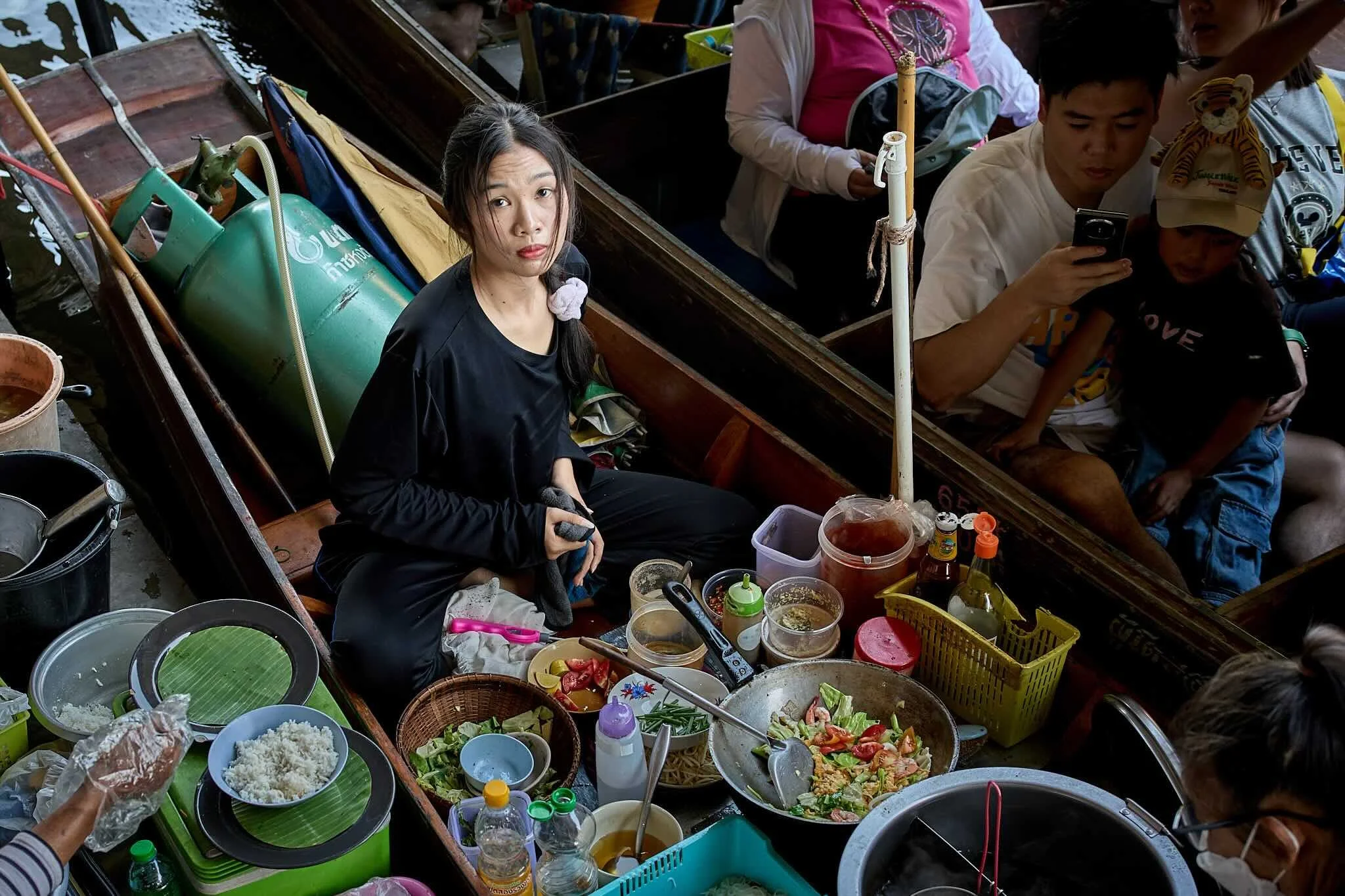 People on a boat enjoying a meal with various dishes, vegetables, and drinks around them.