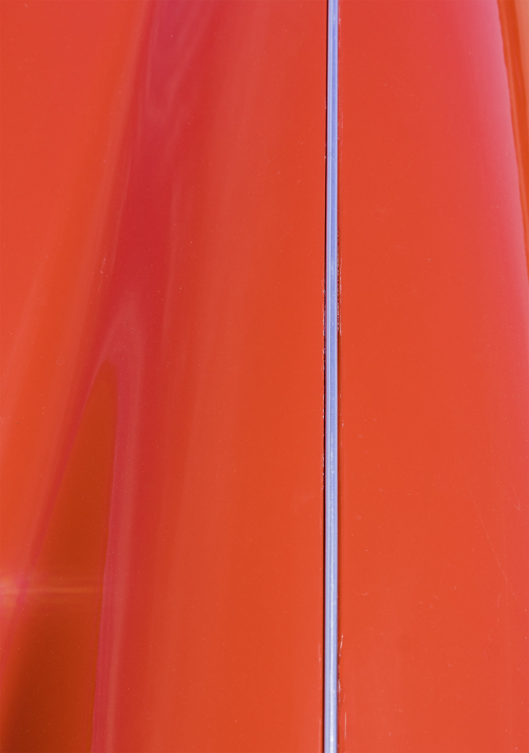 Close-up of a red sports car hood divided by a thin vertical chrome strip, creating a visual effect reminiscent of Barnett Newman's zip paintings.