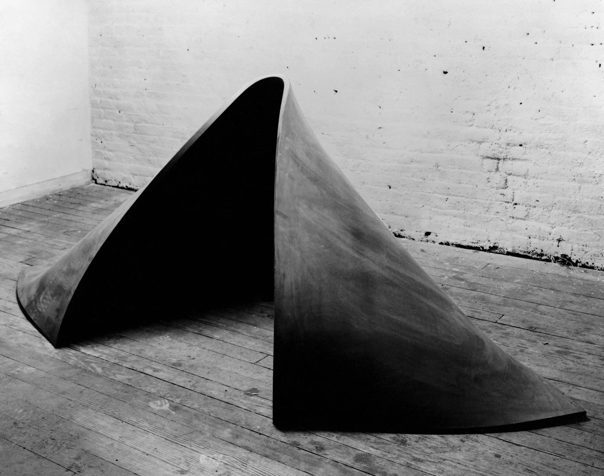 Richard Serra steel sculpture formed from curved industrial plate, emphasizing gravity, weight, and spatial tension through stark minimalist form and darkened surface.