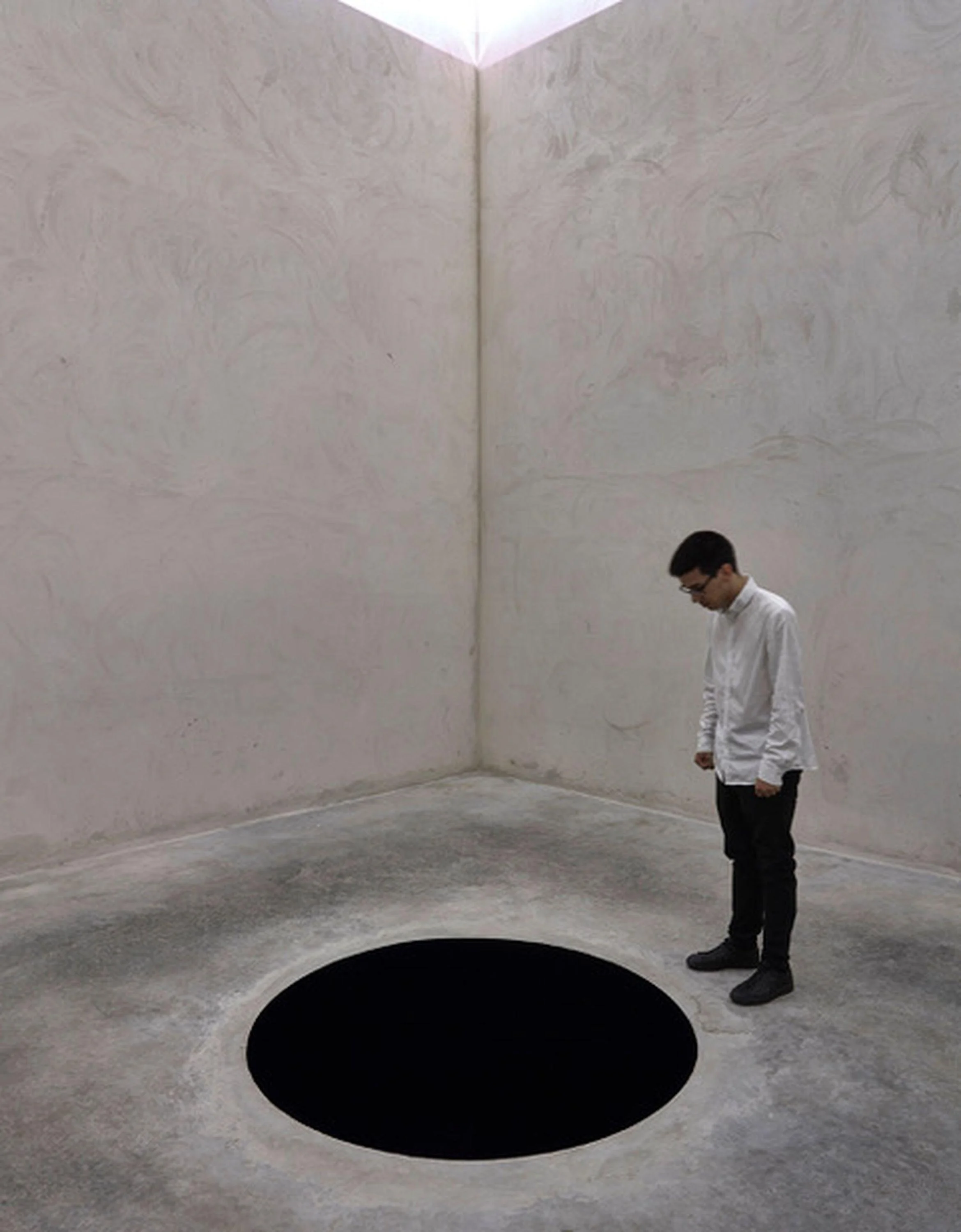 In a room that appears to be made of concrete, a man stares into the blackest of black holes.