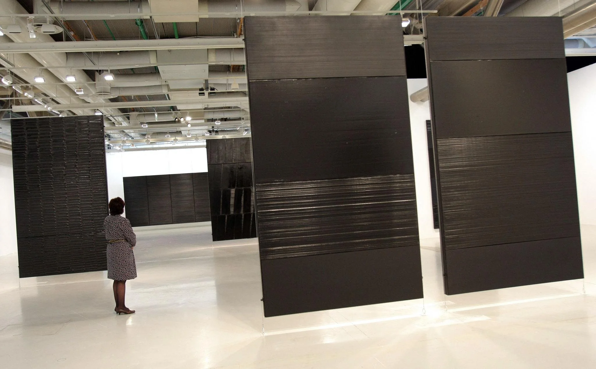 Pierre Soulages Black Paintings hanging with no walls behind them in the Centre Pompidou. A woman stands among them.