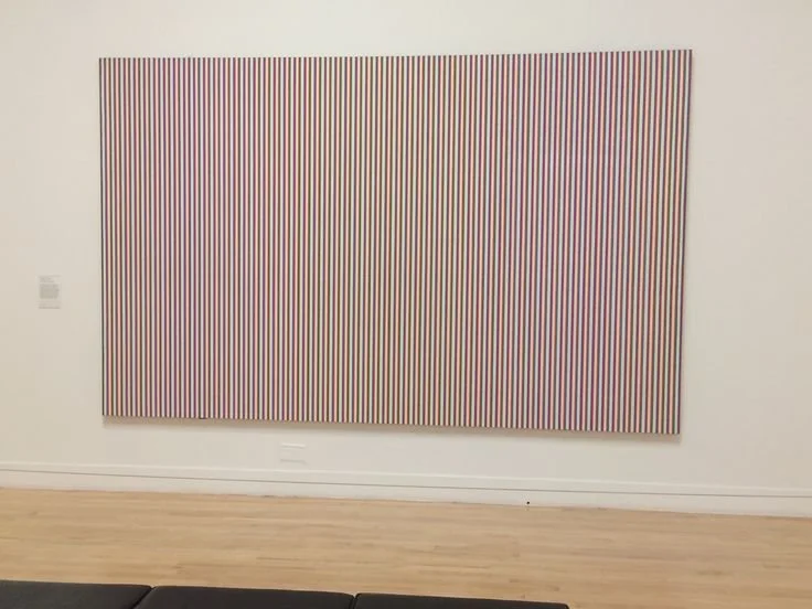 Bridget Riley’s Late Morning is a large horizontal painting composed of narrow vertical stripes in alternating bands of blue, green, red, pink, and violet.