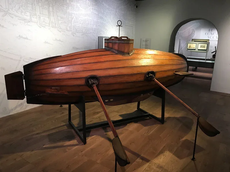 A prototype of a submarine made in wood and leather with two oars coming out of the sides.