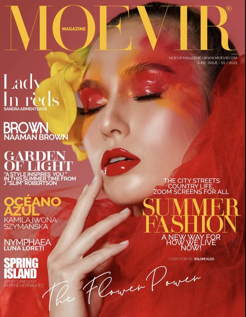 A woman with eyes closed, vibrant red makeup, red lipstick, and a red sheer fabric around her shoulders. She has a yellow flower in her hair. The magazine cover includes various headlines about fashion, summer, and floral themes.