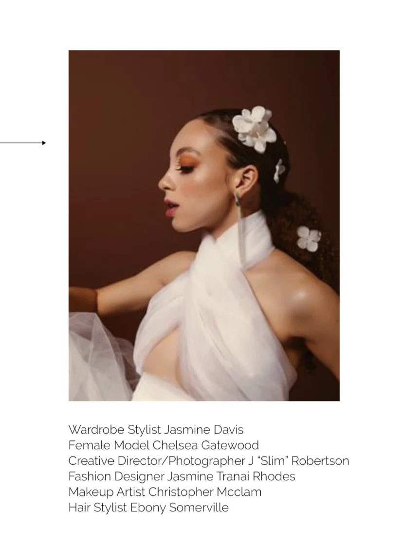 Portrait of a woman with floral hair accessories and makeup, wearing a white dress, against a brown background.