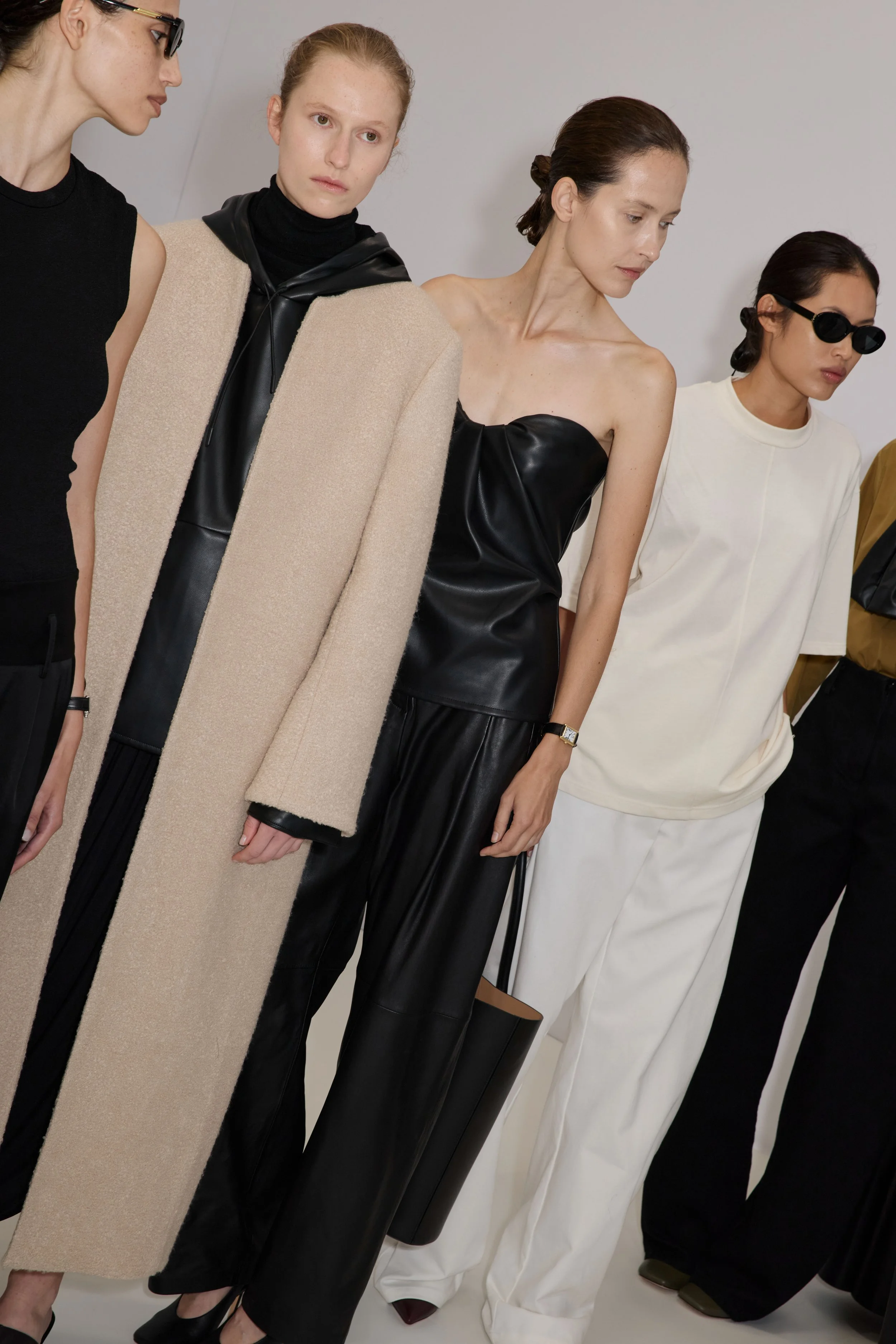 Fashion models in various outfits standing in a row, with focus on their clothing and accessories.