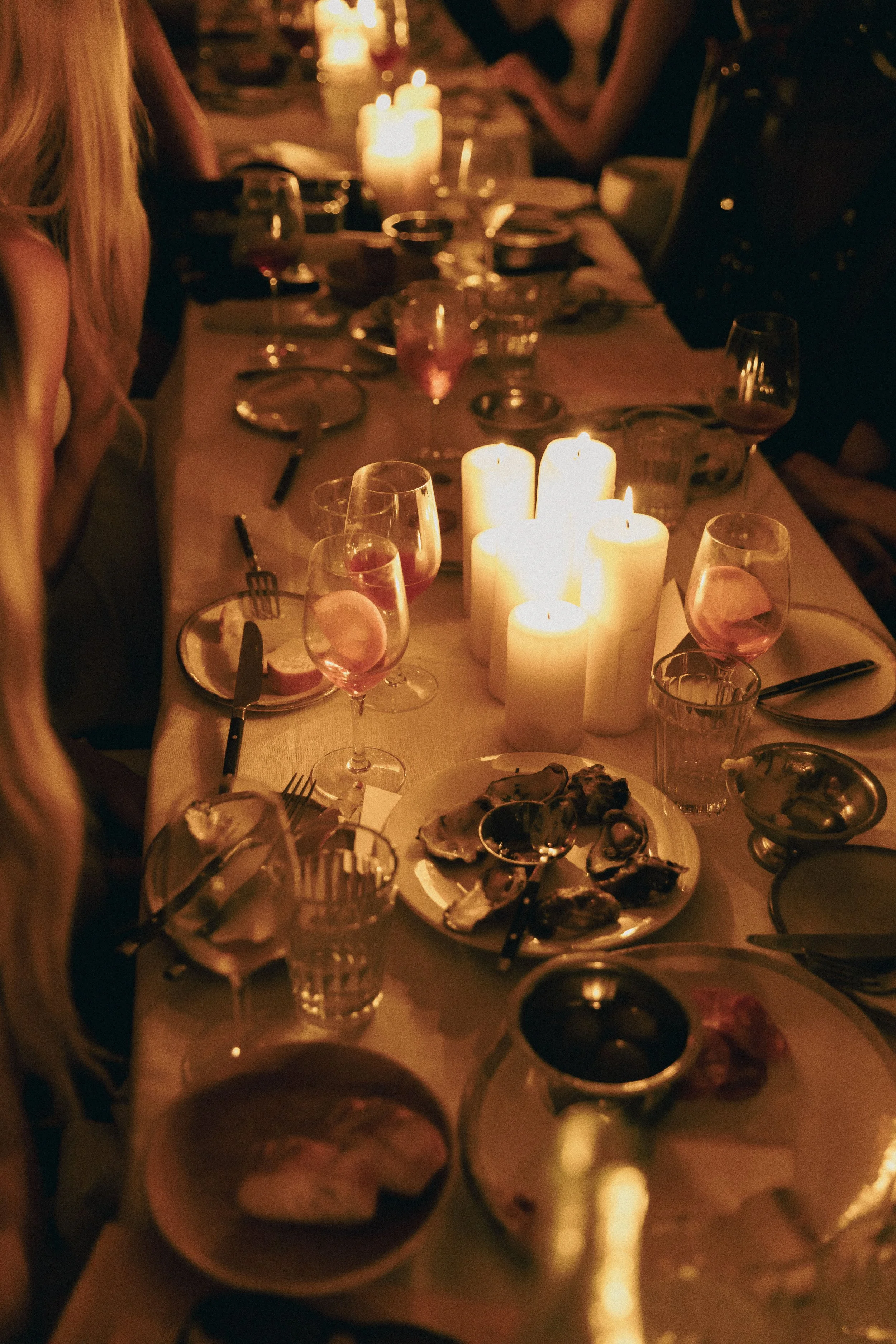 A dinner table with lit candles, wine glasses, plates, and seafood, set for a meal in a dimly lit room.