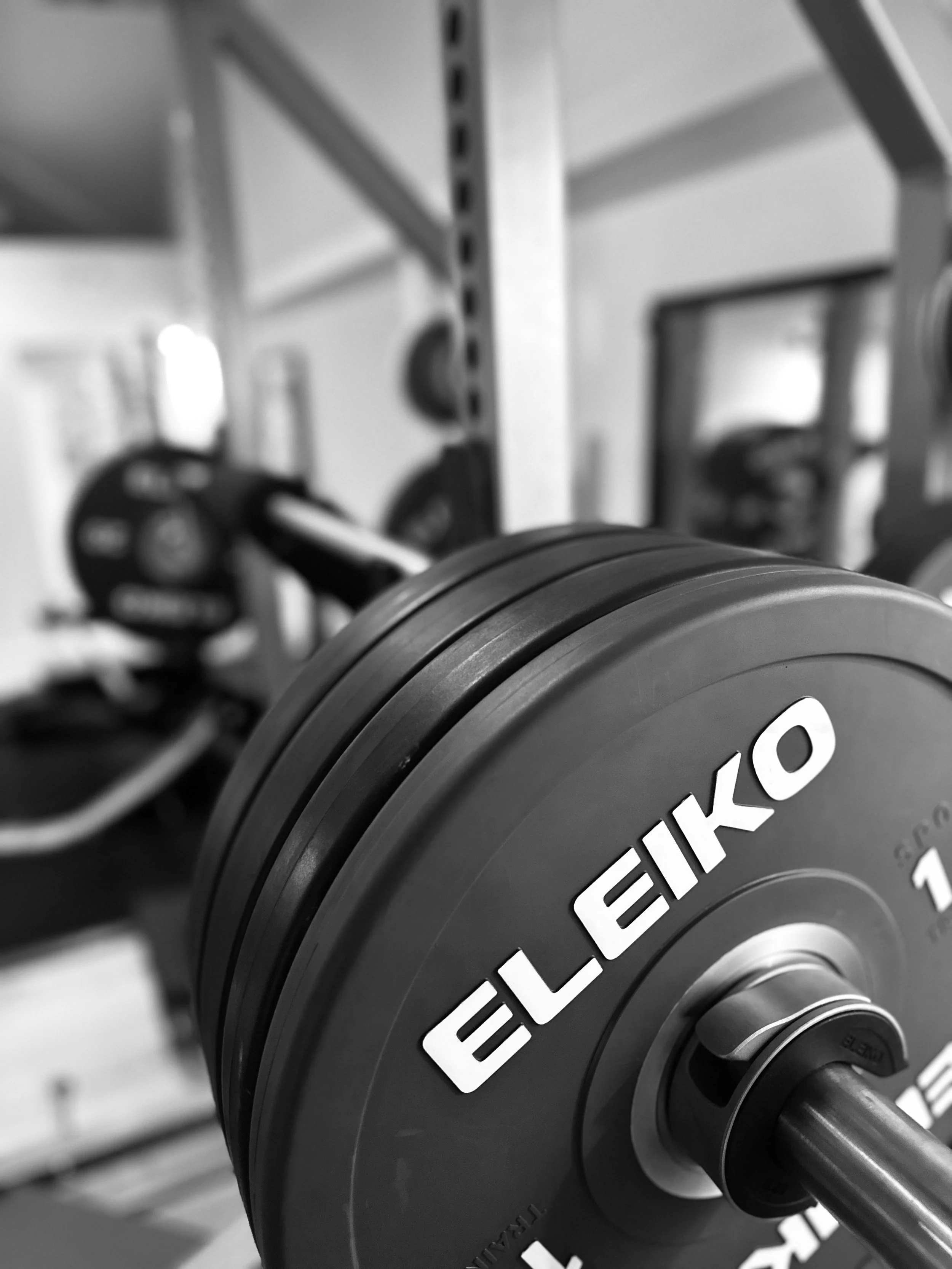 Stacked weight plates on a weightlifting stand with a weightlifting barbell, including 20 kg, 10 kg, and 5 kg plates, in a gym setting.