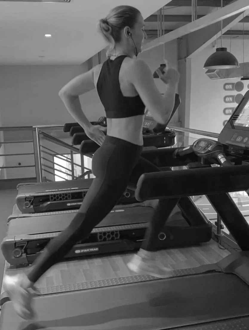 A woman in workout clothes running on a treadmill at the gym, listening to headphones.