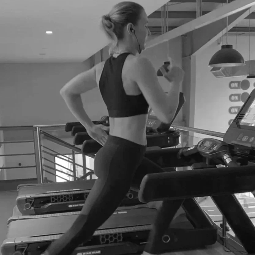 A woman in workout clothes running on a treadmill at the gym, listening to headphones.