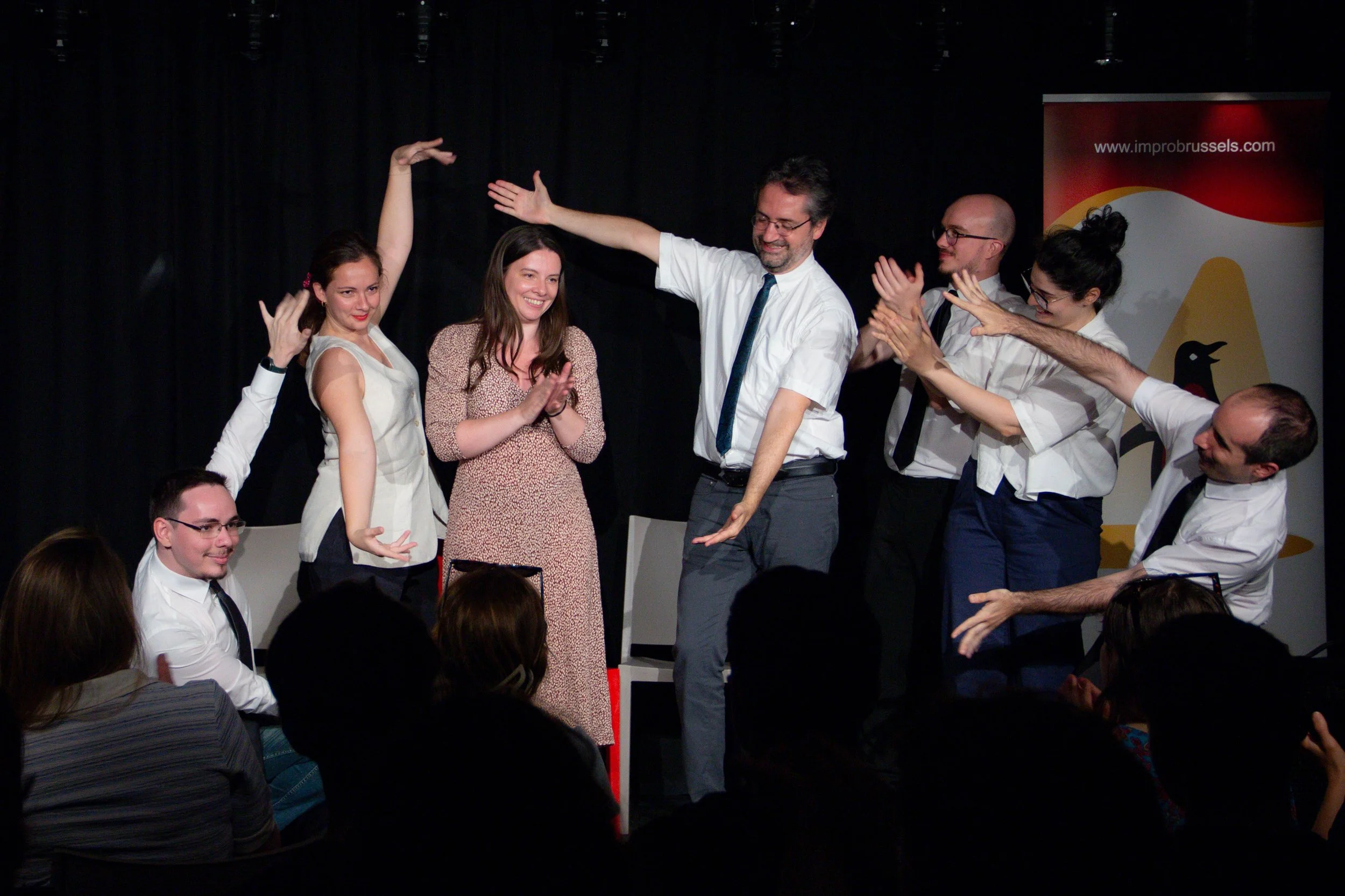 Group of people on stage celebrating, clapping, and smiling during an event with a banner in the background.