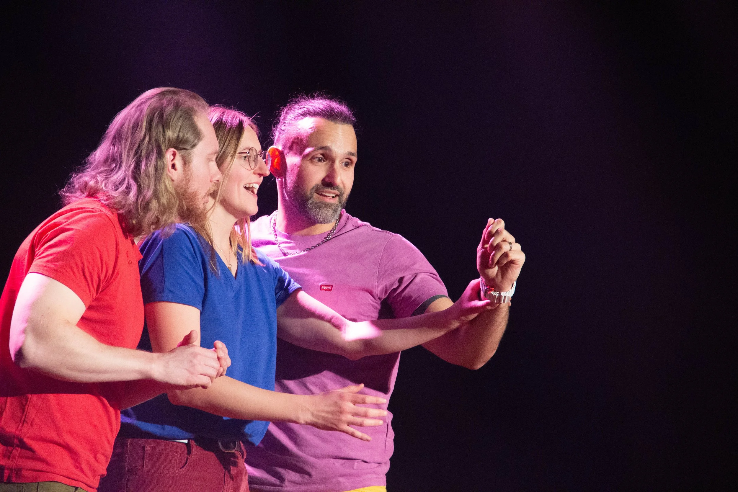 Three people, two women and one man, are looking at a smartphone screen together on a dark stage with purple lighting.