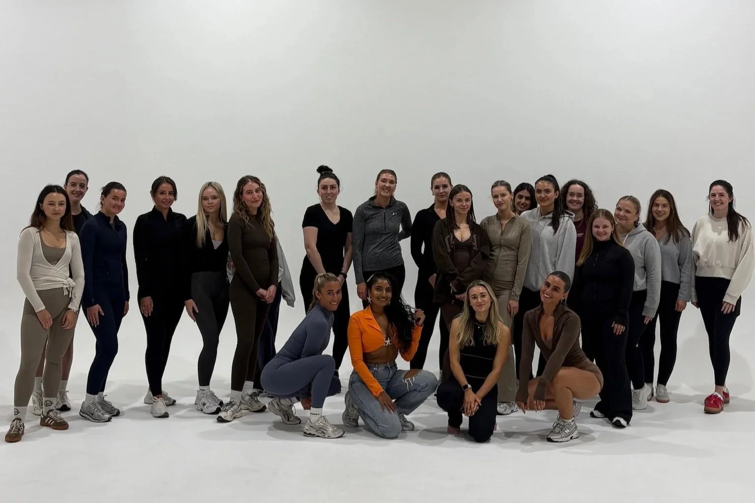 Group of 20 women standing and kneeling in a studio with a plain white background.