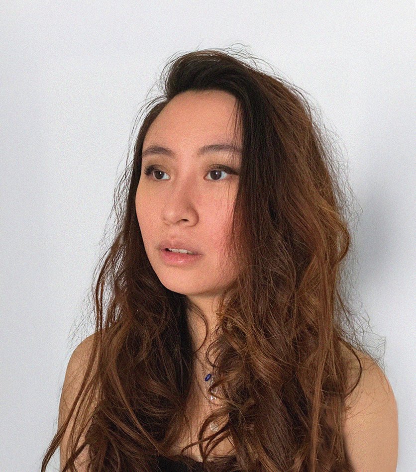 Jeune femme aux cheveux longs et bouclés, regardant légèrement vers la gauche, avec un fond blanc.