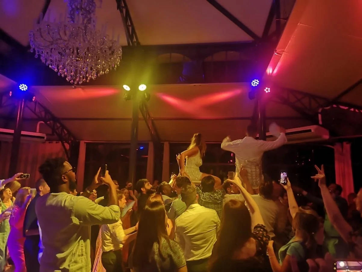 People dancing and taking pictures at a party with colorful lights and a chandelier.