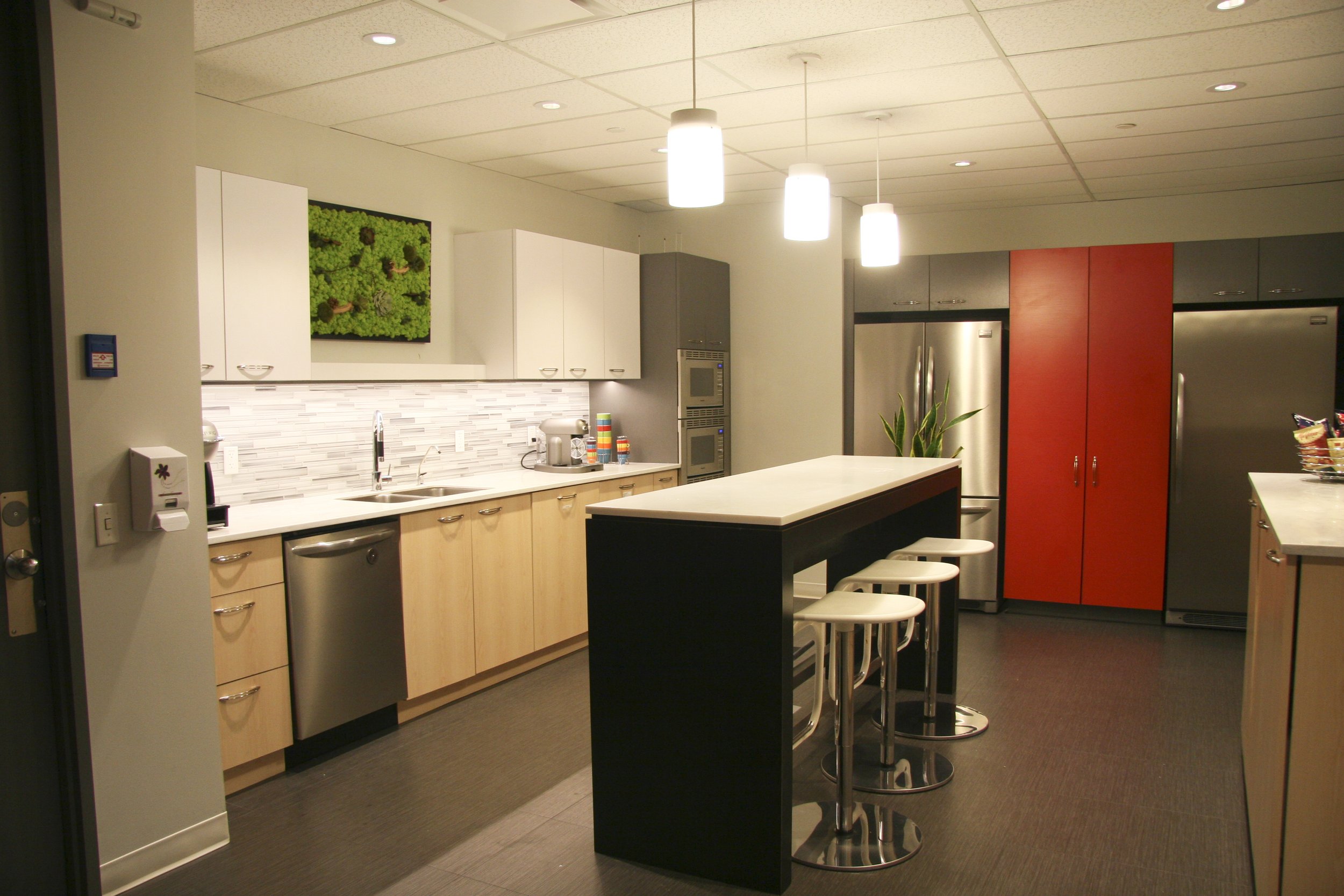 Modern kitchen with a long island, bar stools, stainless steel appliances, and bright ceiling lights.