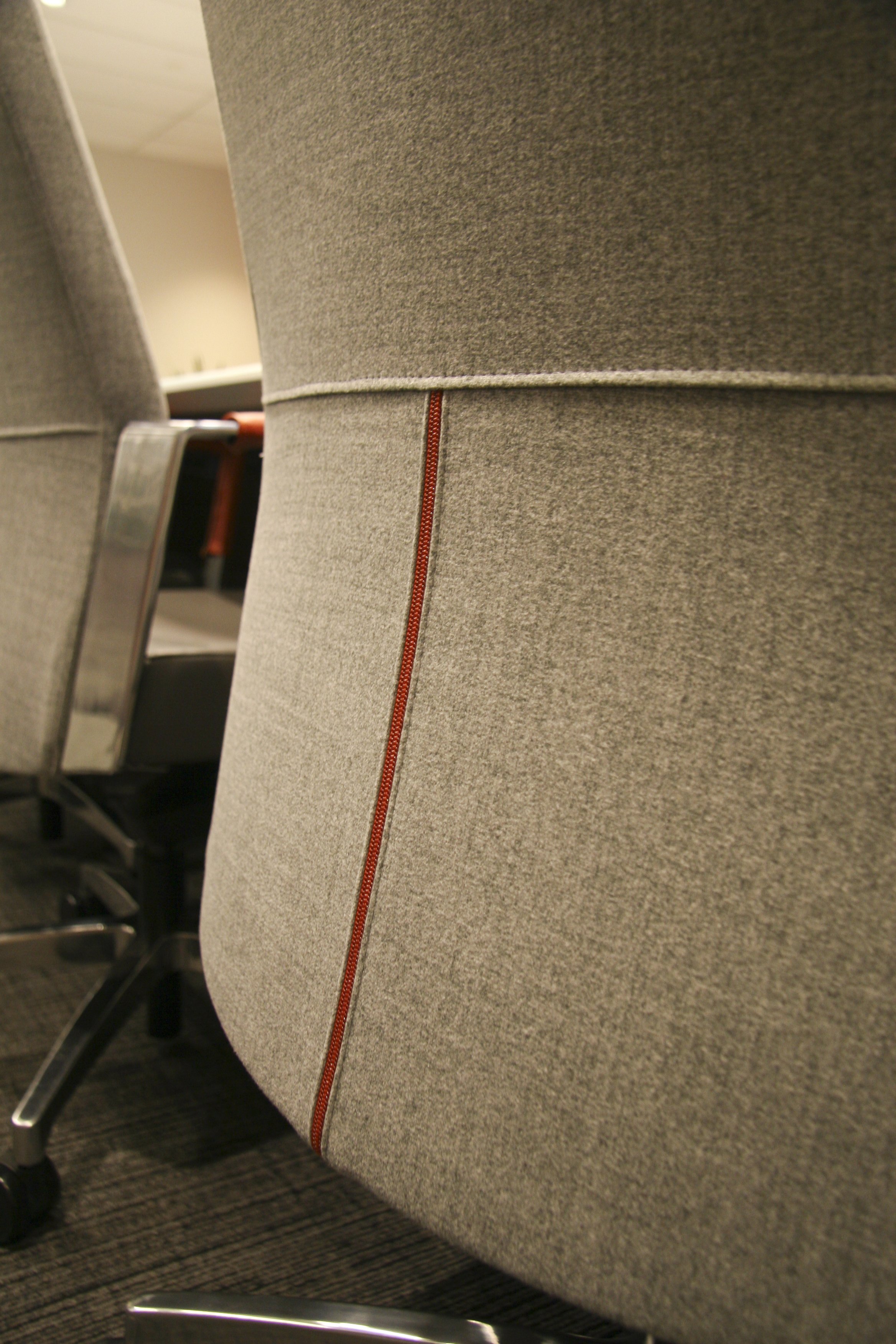 Close-up of a gray office chair with red stitching detail, focusing on the backrest.